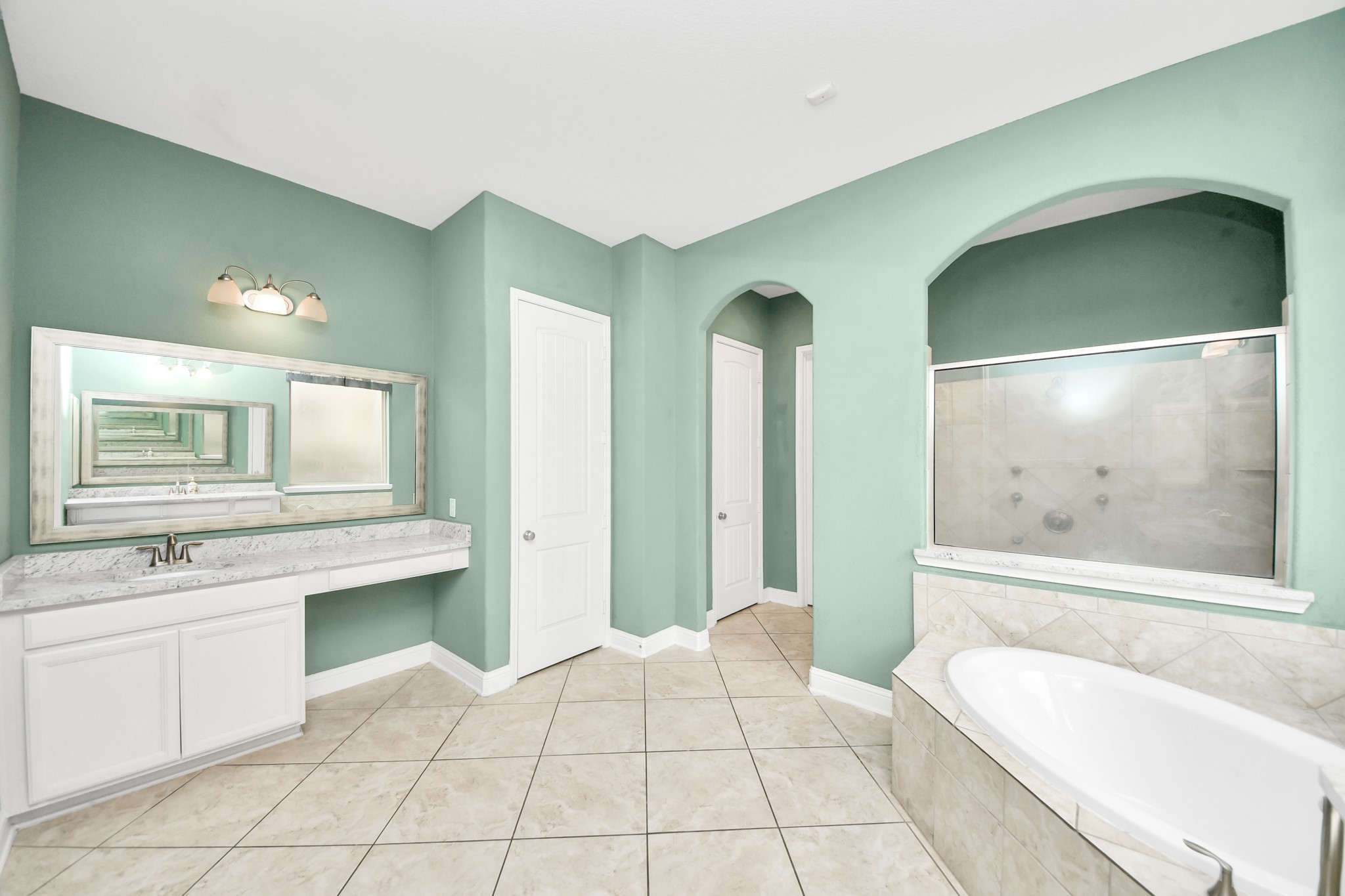 Relaxing primary bath with a tiled soaking tub, expansive vanity, oversized mirror, and separate shower.