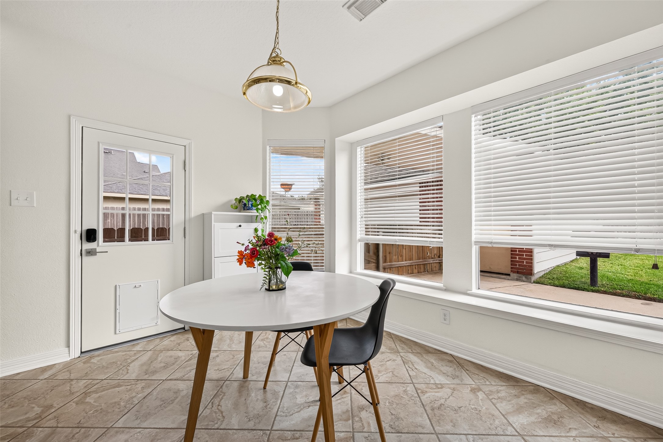 Bright breakfast nook featuring large windows with blinds, a stylish round table, and modern chairs, offering a cozy spot with views of the backyard.