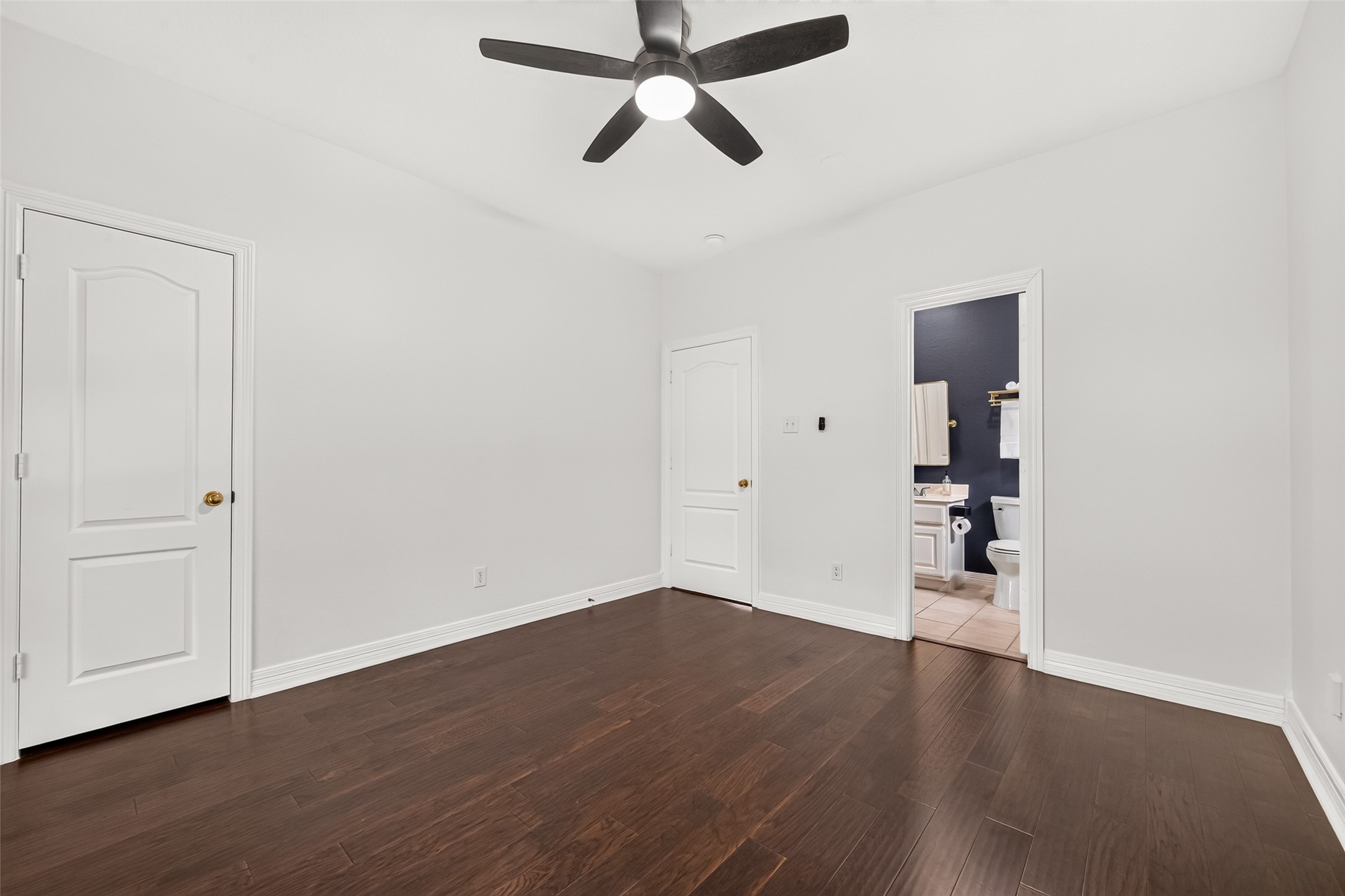 First floor guest bedroom featuring hardwood flooring, ceiling fan, and convenient ensuite bathroom access.