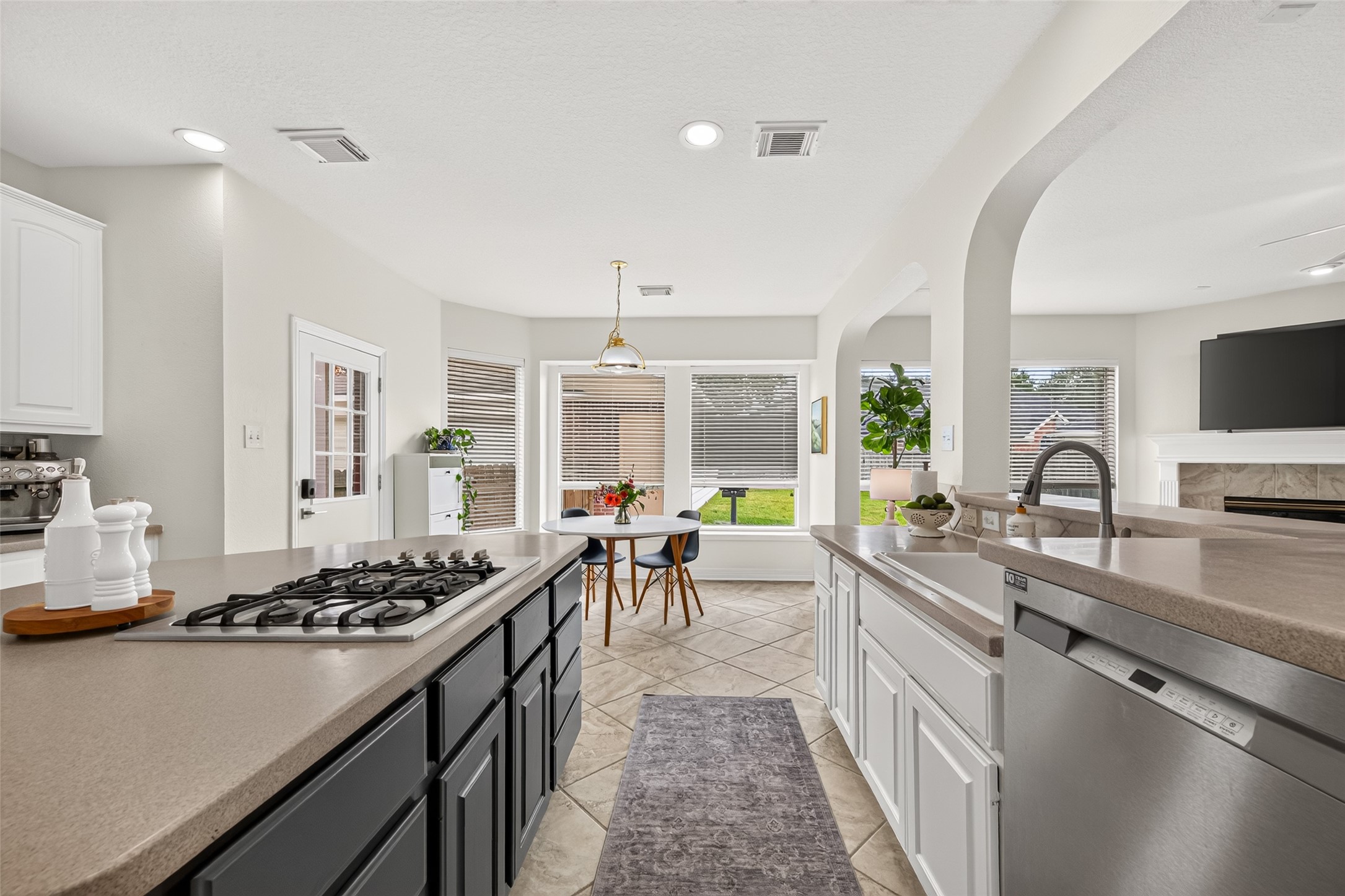 Spacious and modern kitchen with sleek countertops, a gas cooktop, and stainless steel appliances. Sunlit dining area with large windows offers a cozy breakfast nook, while the open layout seamlessly connects to the living room featuring a fireplace.