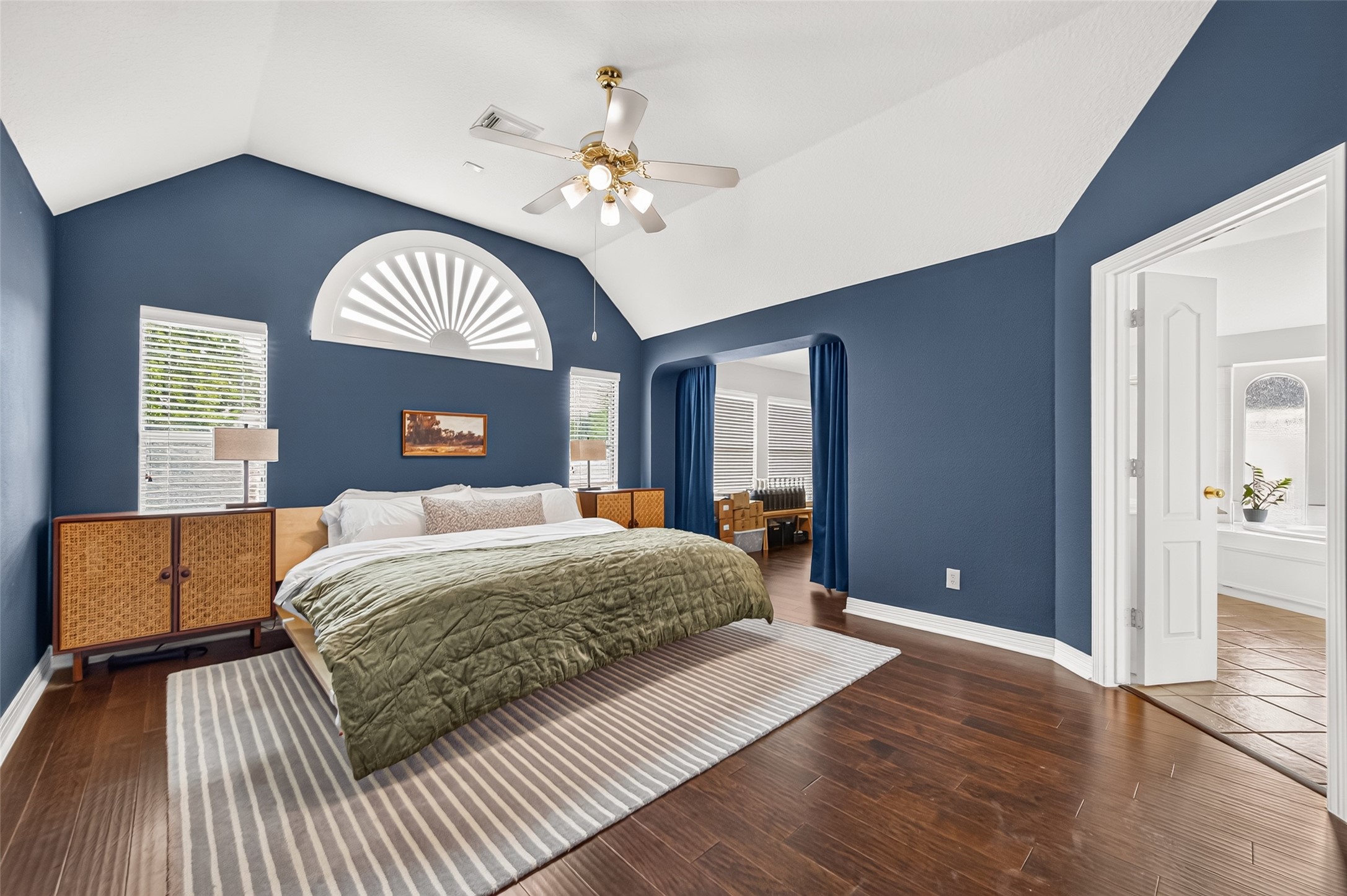 Primary bedroom featuring vaulted ceilings, rich hardwood flooring.
