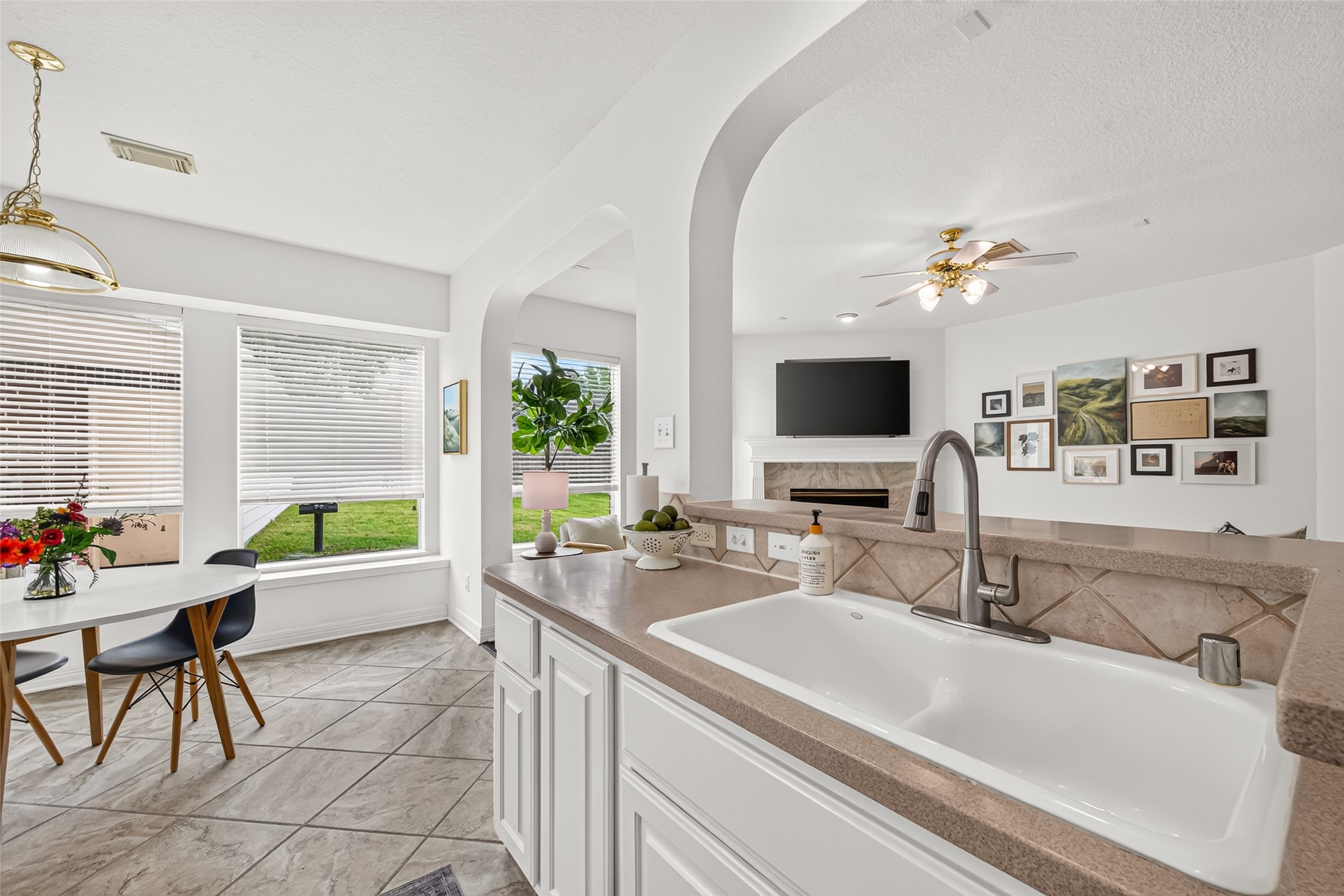 Bright and inviting open-concept kitchen and living area with elegant tile flooring, a cozy fireplace, and abundant natural light from large windows.