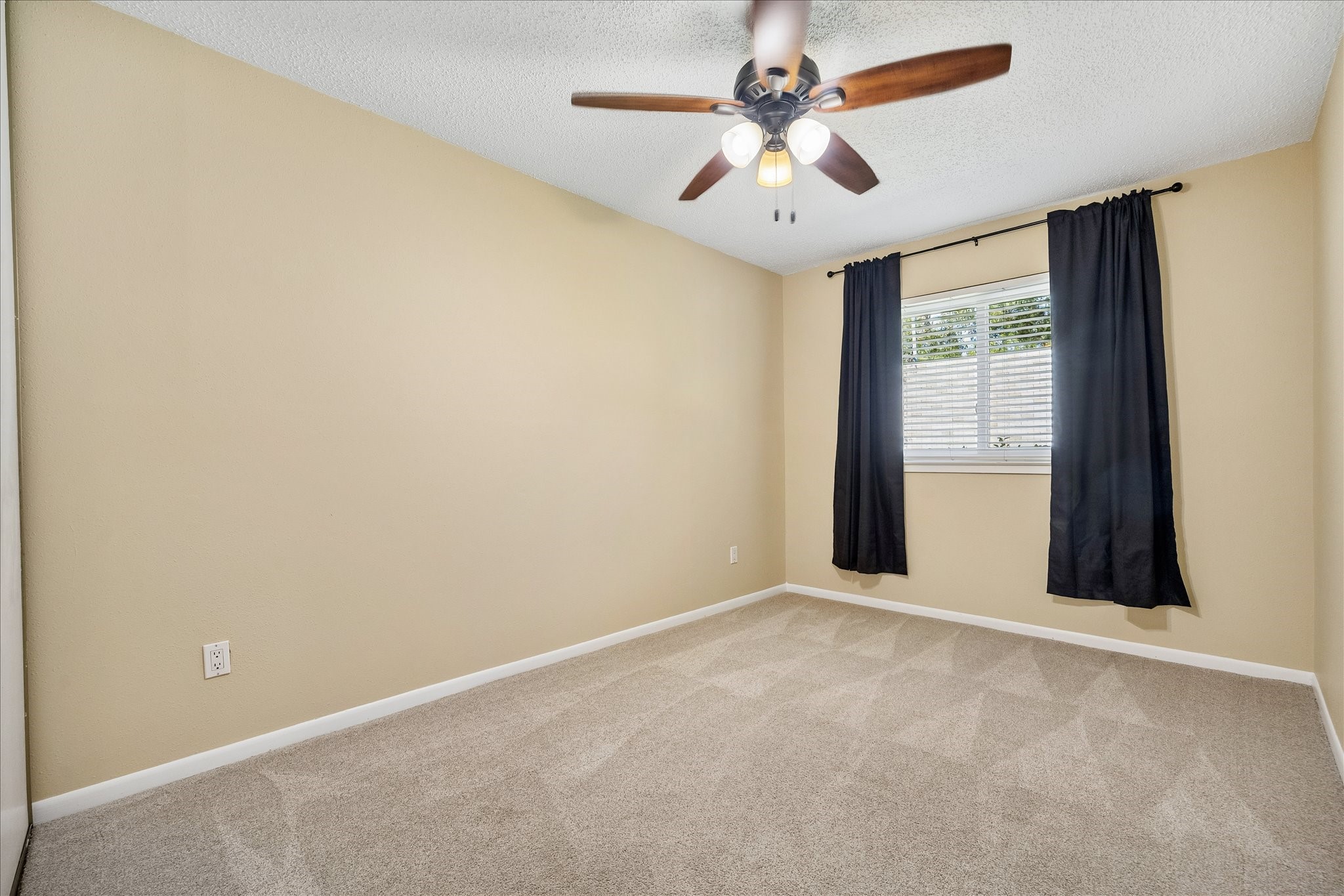 Settle into this inviting bedroom with soft carpeting, a ceiling fan, and a window dressed with curtains for a comfortable feel.