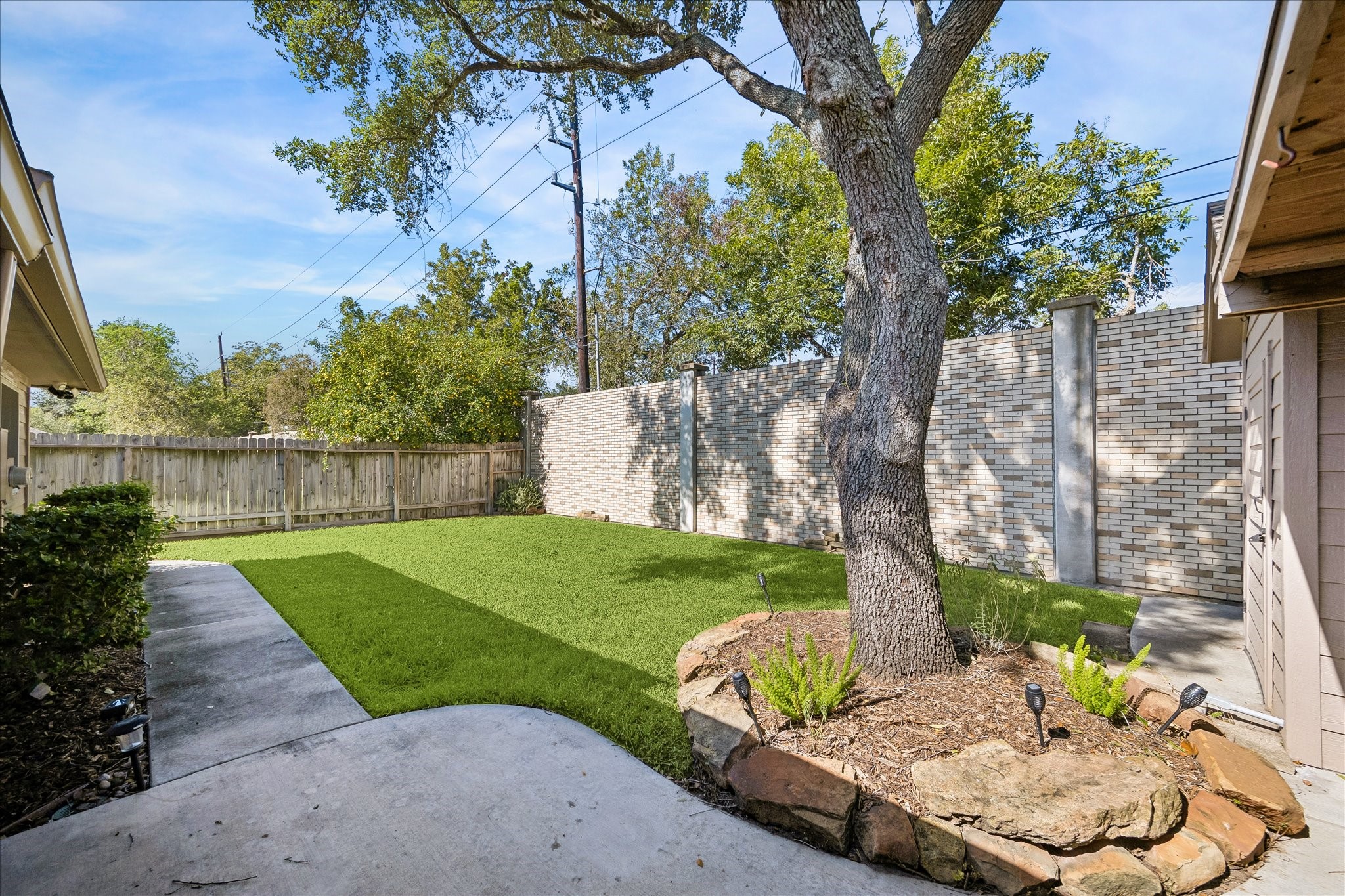 Enjoy your own fenced backyard with a grassy lawn, mature shade tree, and a charming stone-edged garden area.