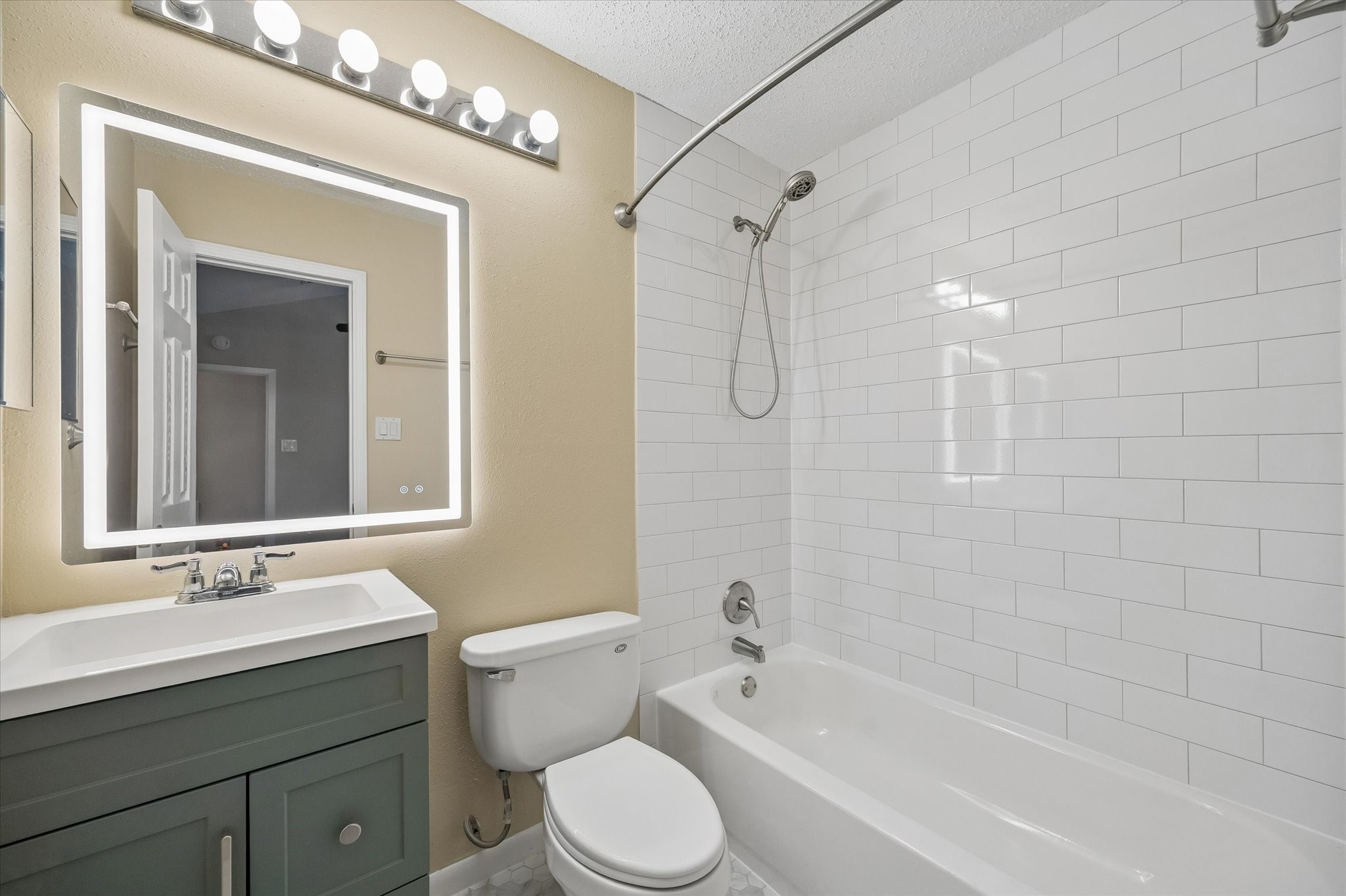 Start and end your day in this refreshed bathroom featuring a stylish green vanity, bright mirror, and classic subway tile.