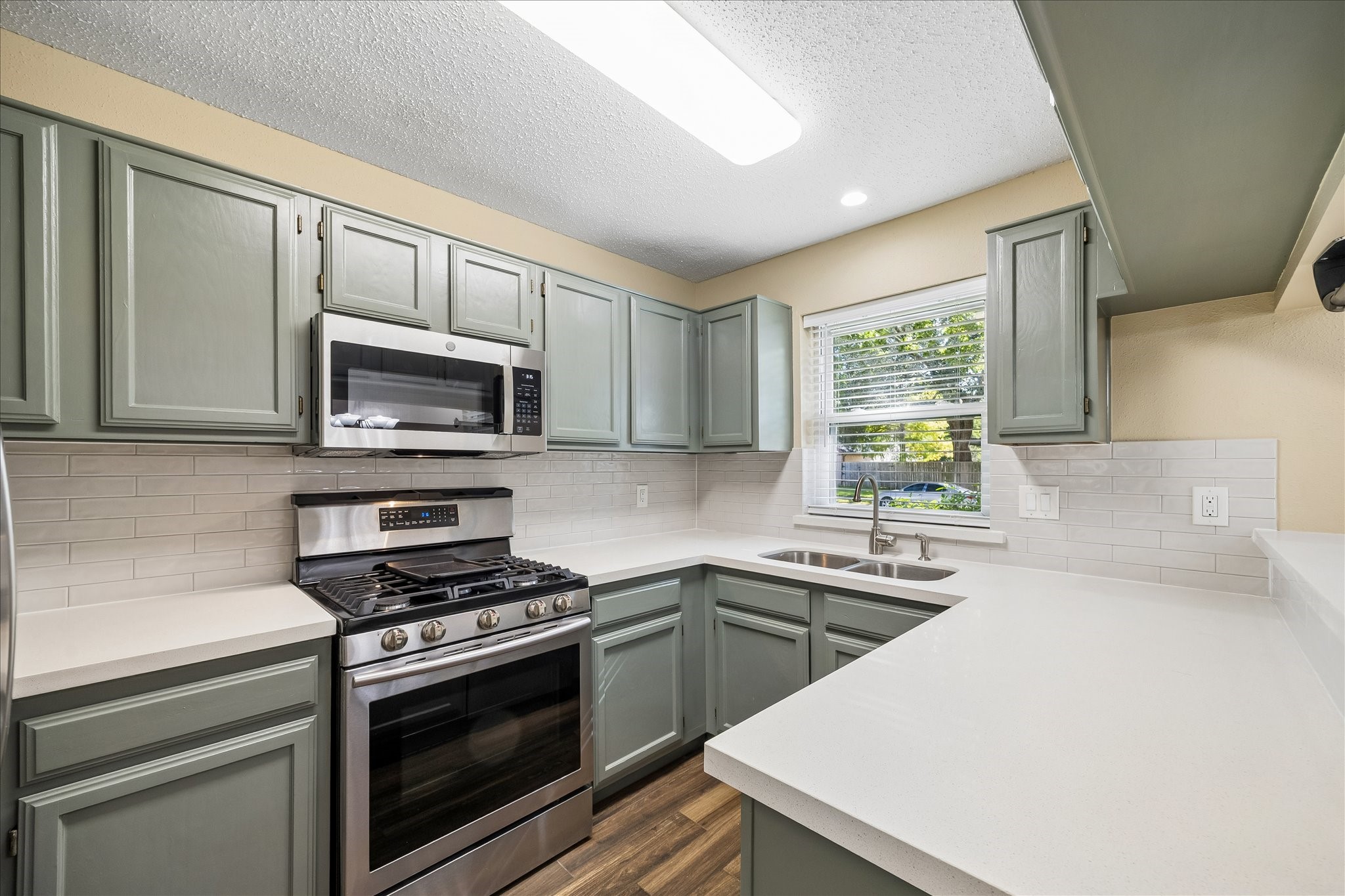 A kitchen you'll love coming home to! Enjoy attractive sage-green cabinetry, crisp white countertops, subway tile, and stainless steel appliances.