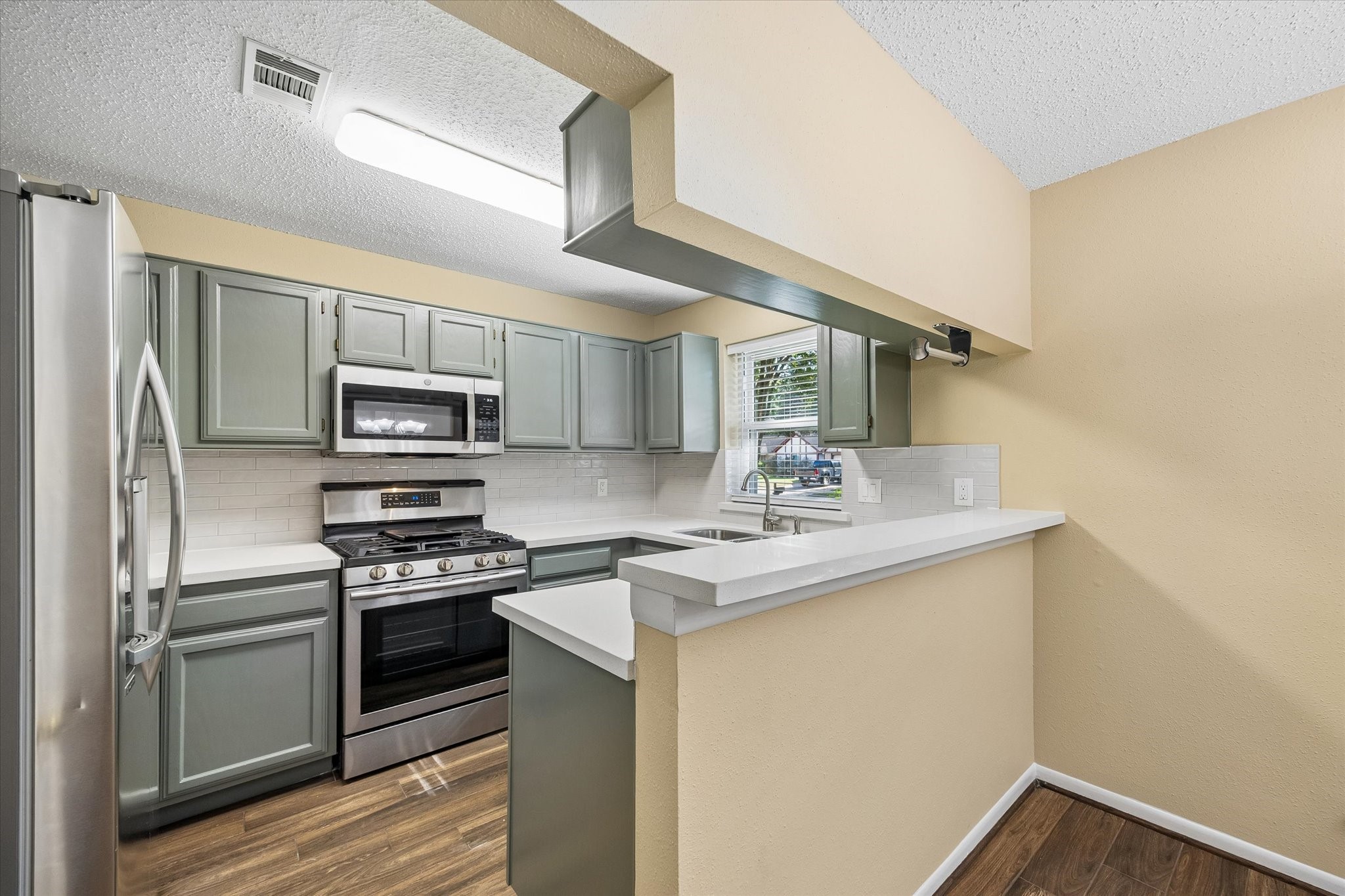 Love to cook? This updated kitchen features stylish sage-green cabinets, stainless steel appliances, and a convenient breakfast bar.