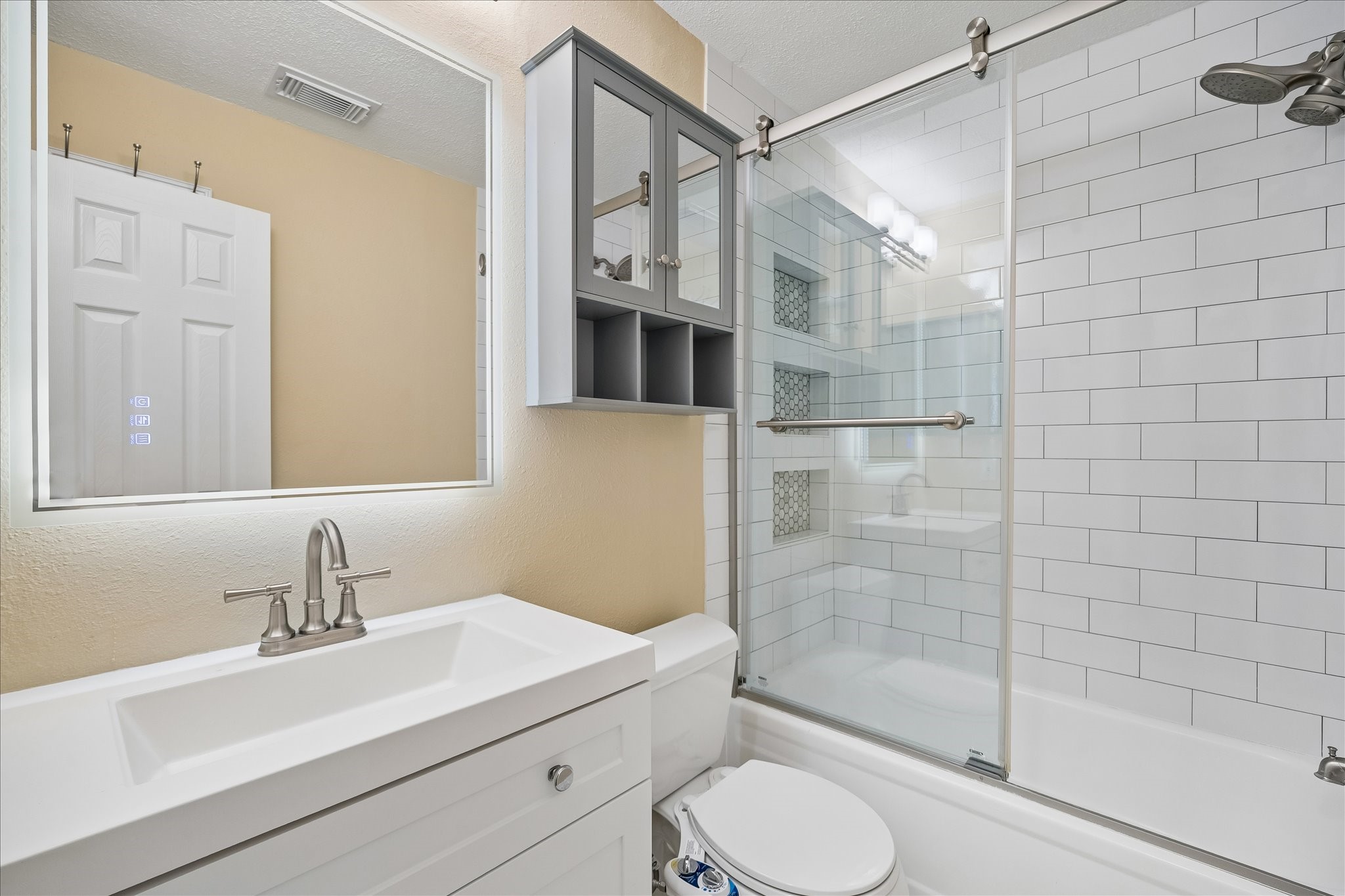 Enjoy a clean, modern look in this updated bathroom with a white vanity, subway tile, and a glass-enclosed tub and shower.