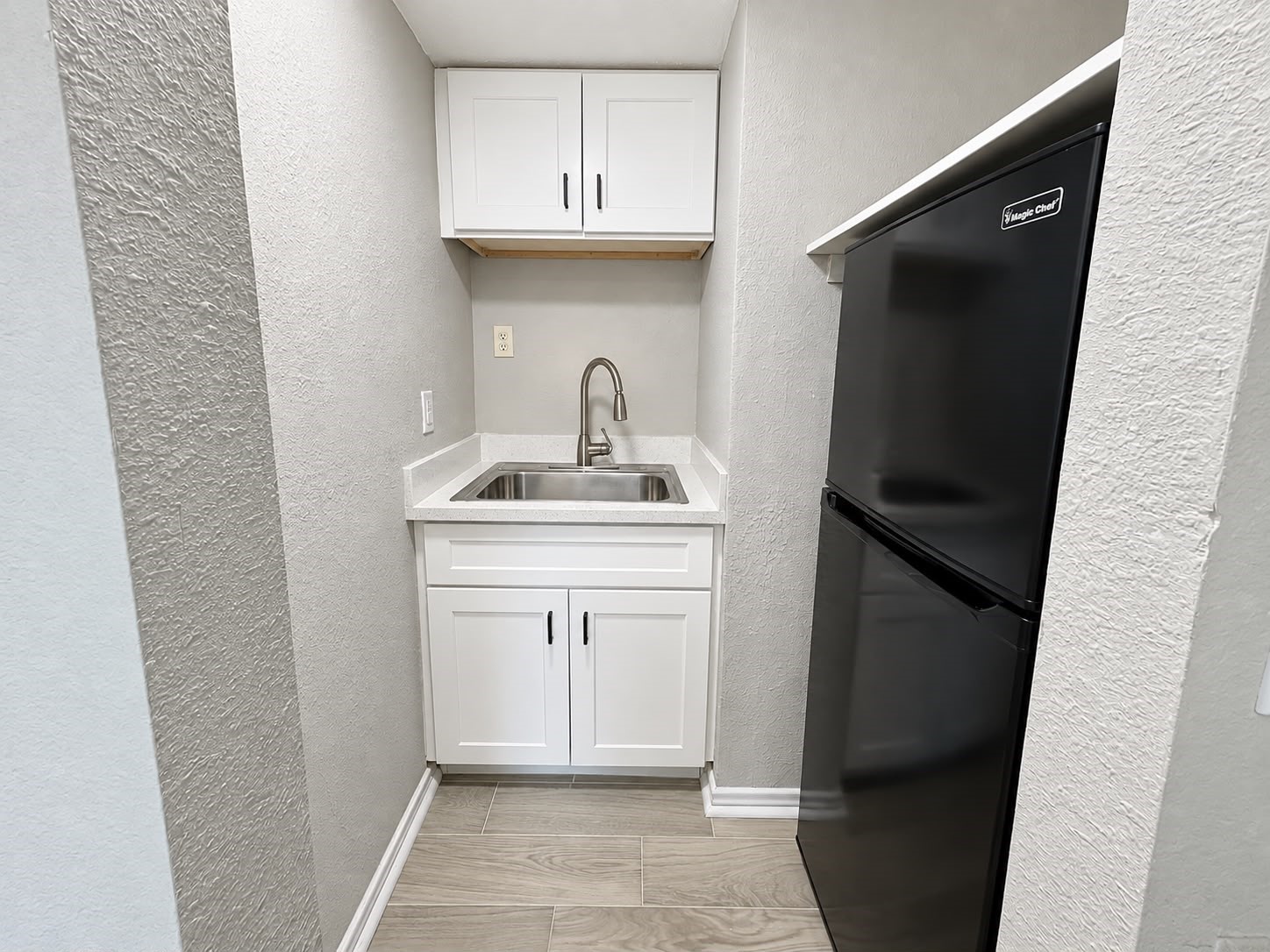 Kitchenette with sink, cabinetry, and refrigerator.