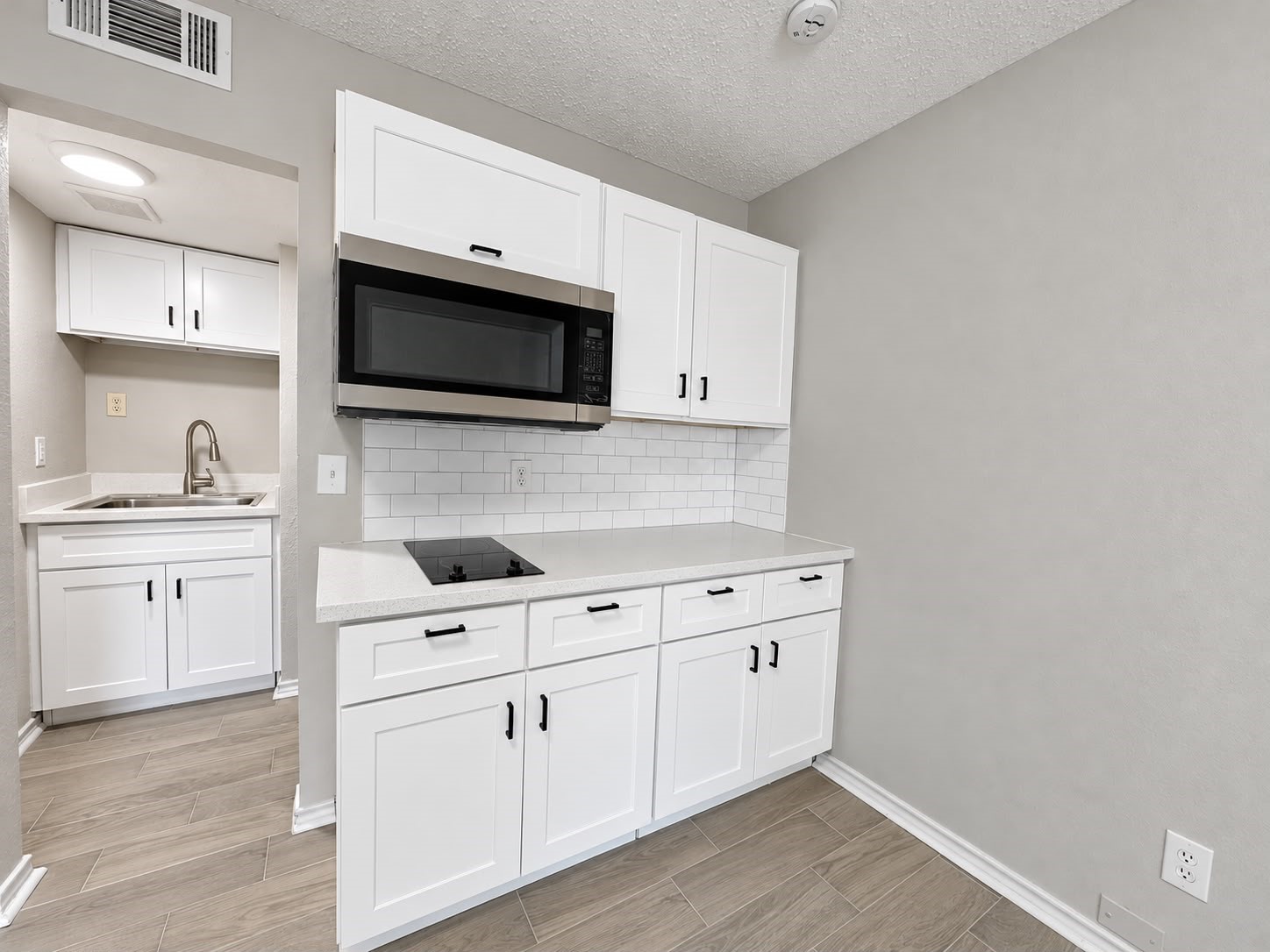 Modern kitchenette with white cabinetry and black hardware.