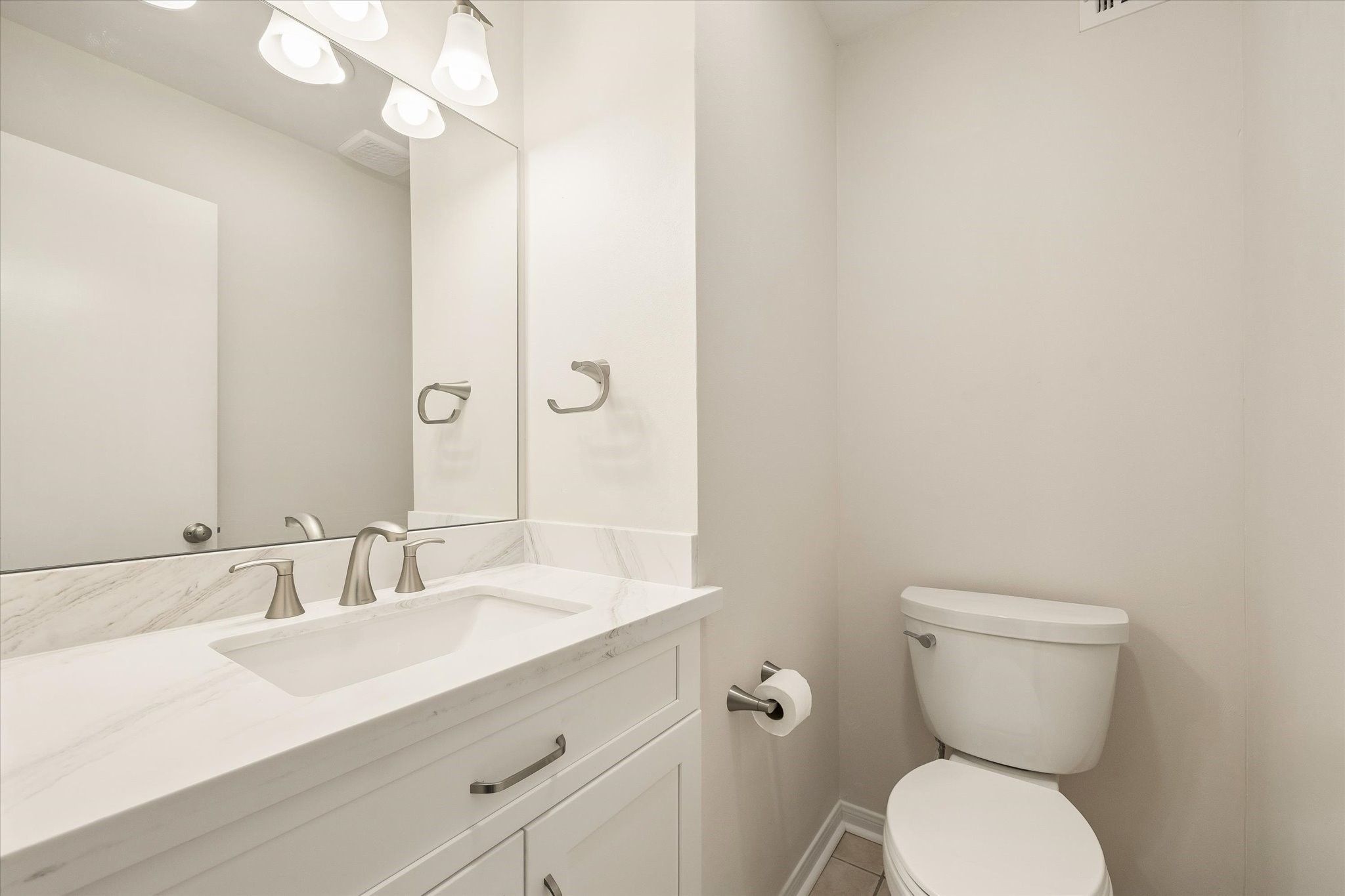 THE HALF BATH FEATURES A WHITE VANITY, STONE COUNTERTOP, UNDERMOUNT SINK, AND BRUSHED-NICKEL FIXTURES.