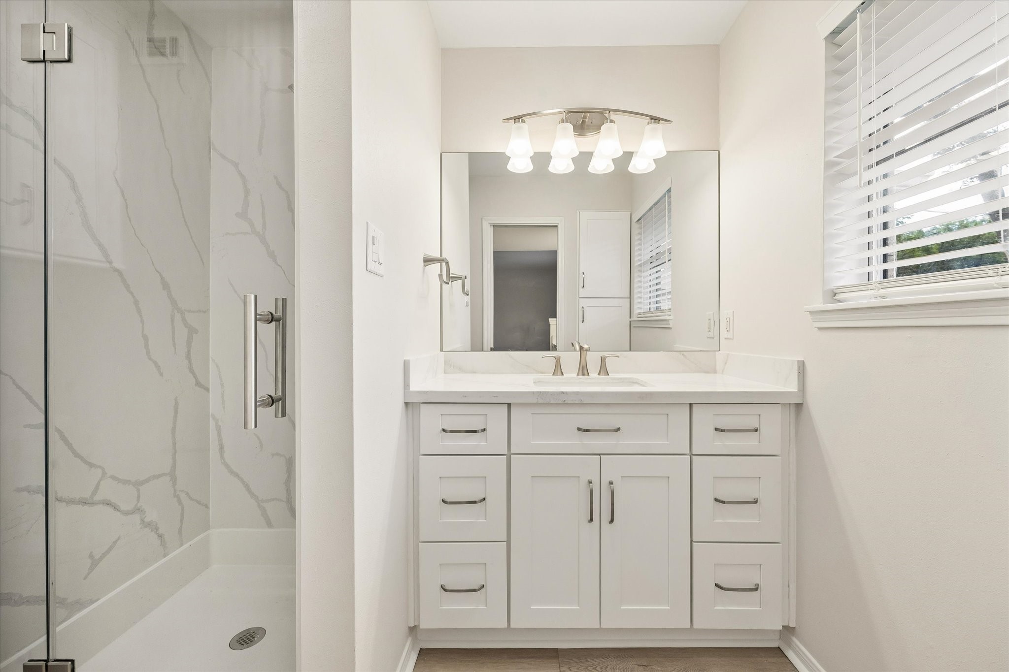 A SPACIOUS PRIMARY BEDROOM FEATURES NEUTRAL FINISHES, A CEILING FAN, AND A WIDE WINDOW WITH TREE-LINED VIEWS.