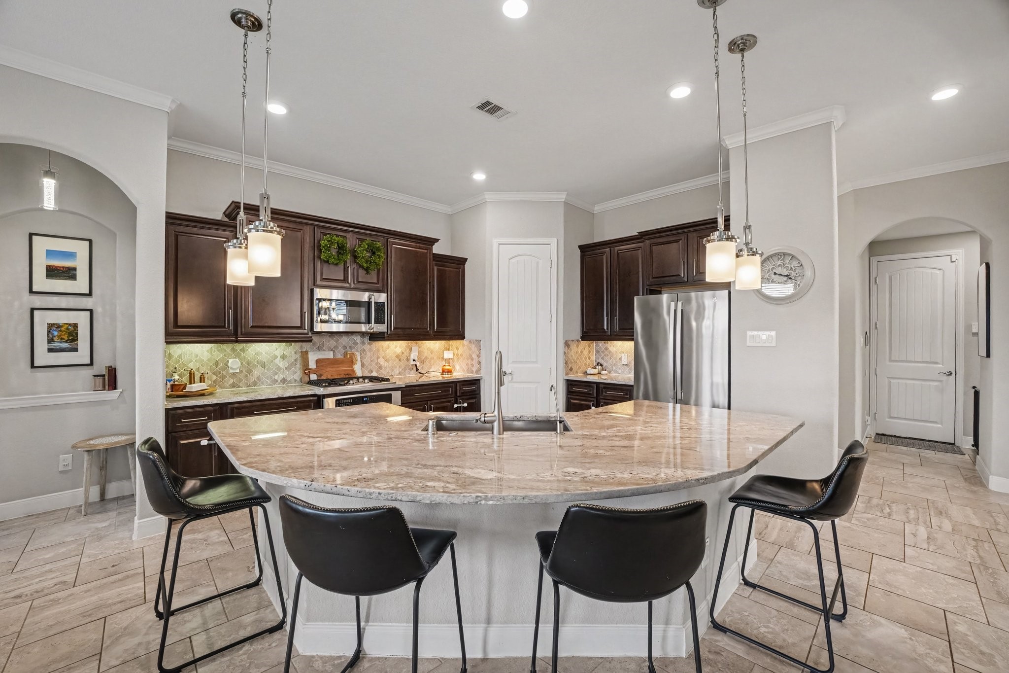 At the centerpiece is a expansive, curved granite island illuminated by stylish pendant lights, featuring an undermount sink, goose-neck faucet, and comfortable bar-height seating.