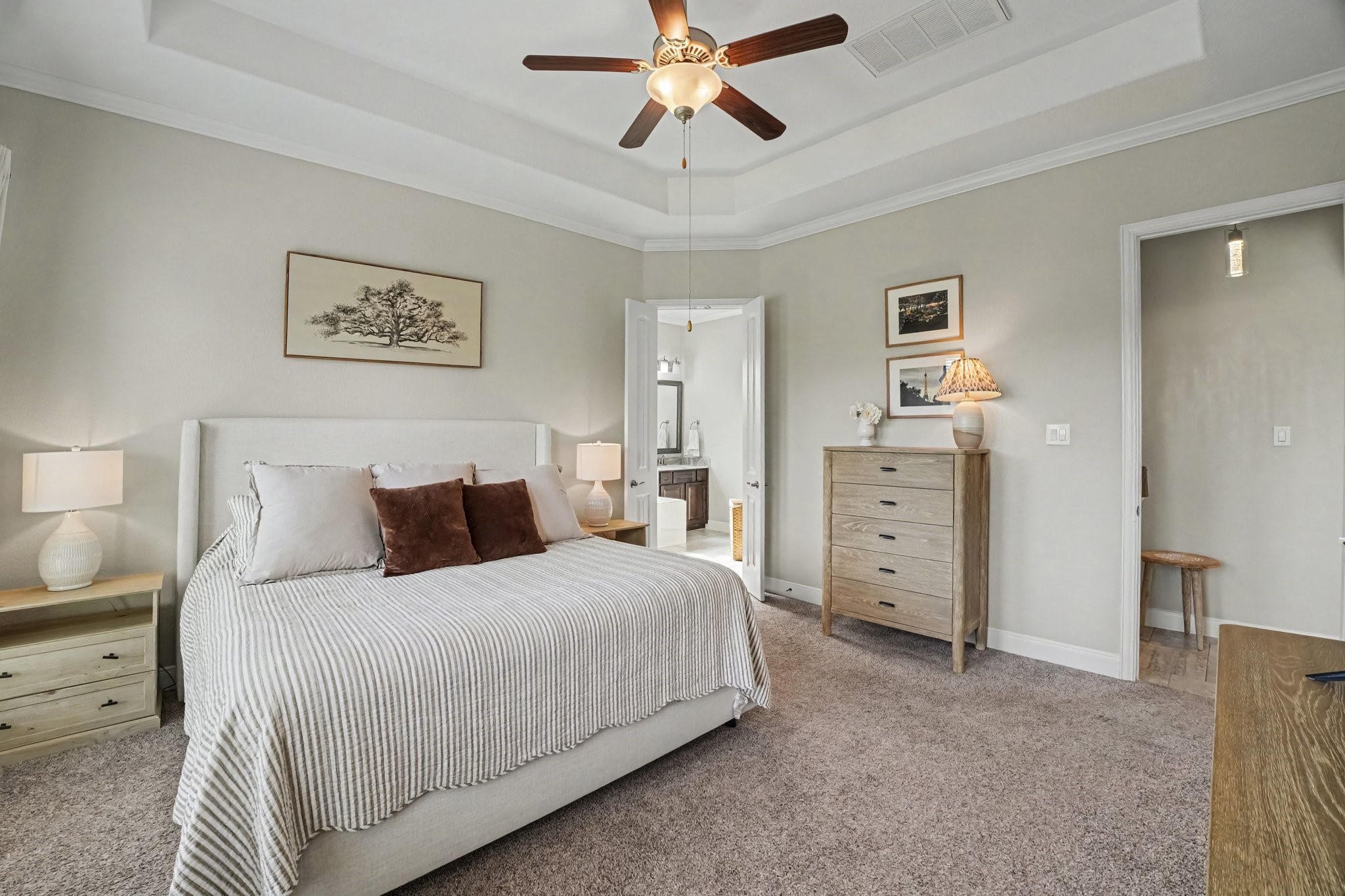 This luxurious primary suite serves as a serene sanctuary designed for ultimate comfort and relaxation. Elegant architectural features elevate the room, starting with an impressive recessed tray ceiling with double crown molding and a classic ceiling fan centered overhead.