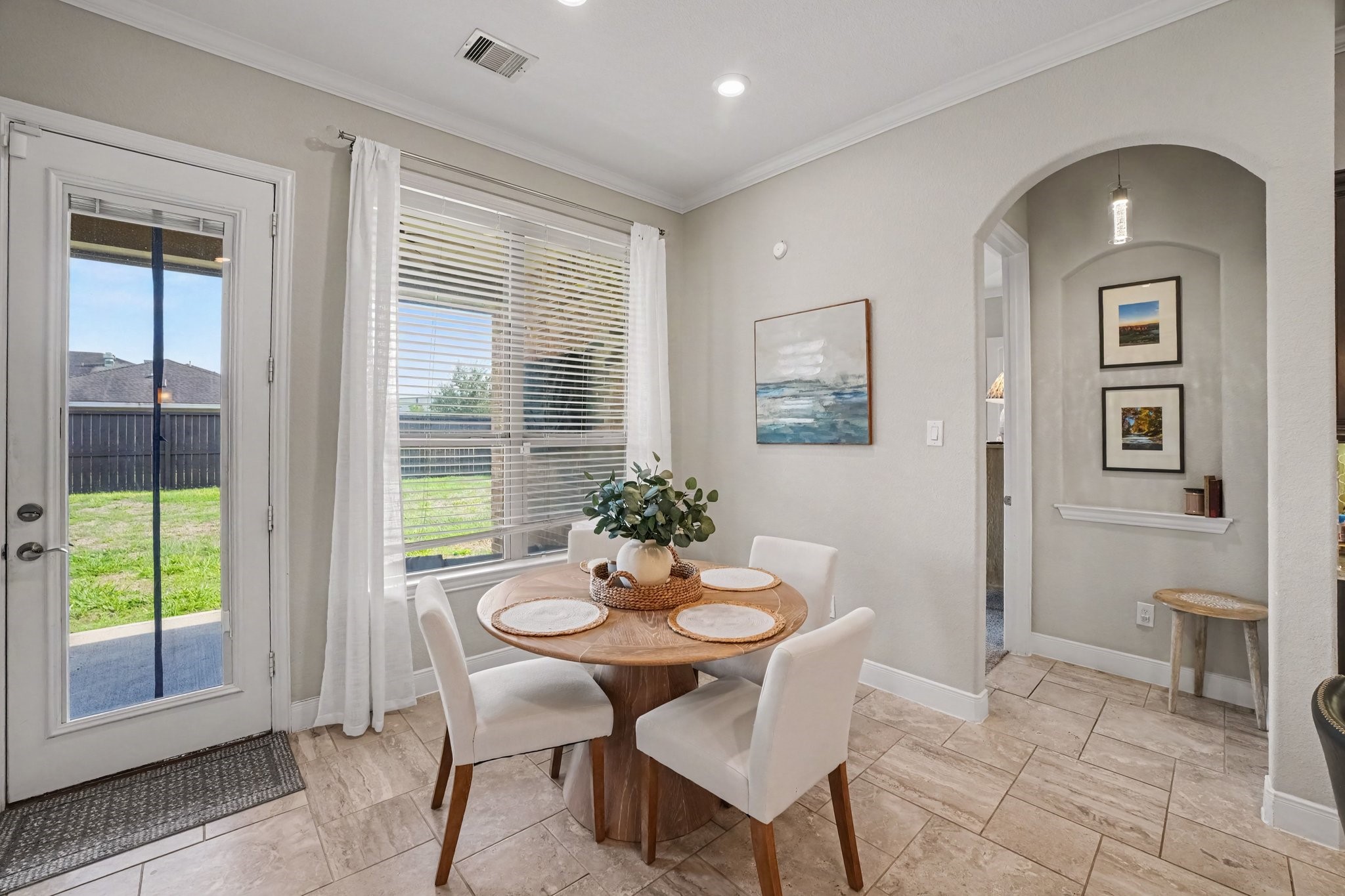 This charming breakfast nook offers a bright and comfortable space for casual daily dining. Positioned alongside a large window with blinds and sheer drapes, the area is bathed in natural light and provides serene views of the backyard. A glass-paneled exterior door gives immediate, convenient access to the outdoor patio space.