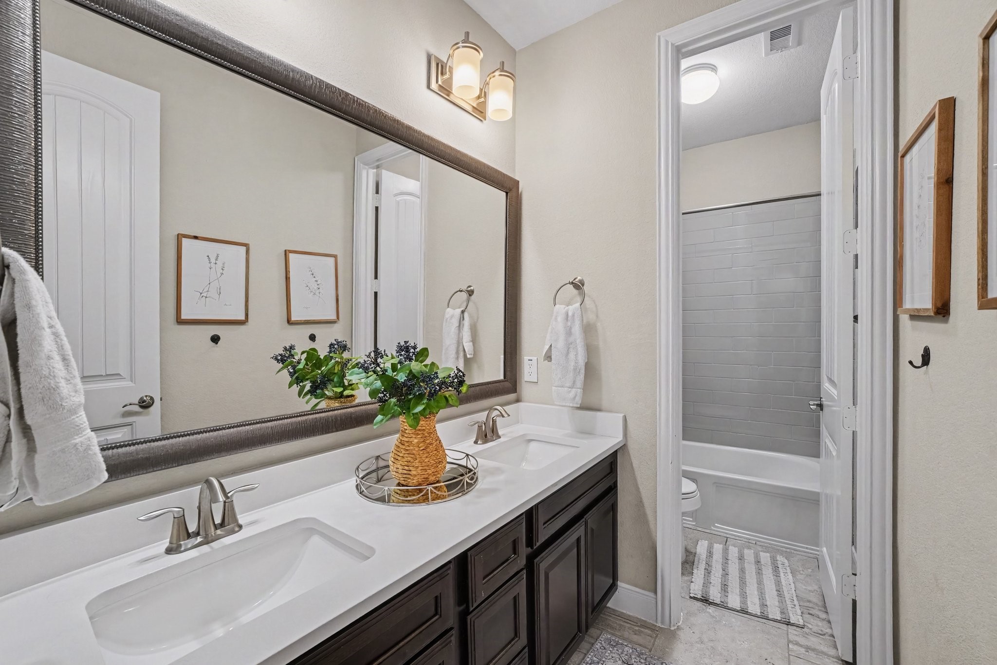 This beautifully appointed full bathroom offers exceptional convenience and modern style for family or guests. Through a separate interior door, the private toilet and shower/tub combination area showcases sleek, grey subway tile surround, ensuring seamless functionality and privacy during busy mornings.
