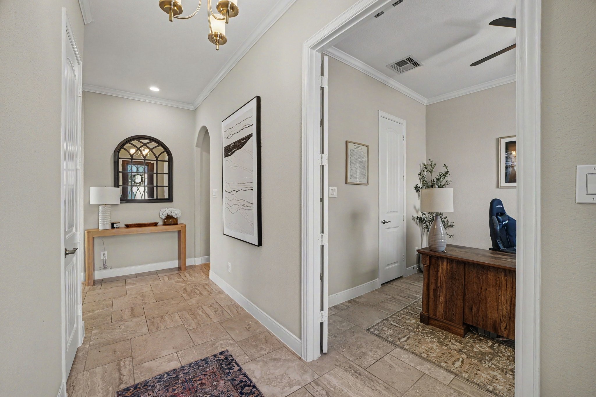 This vantage point highlights the seamless flow and versatile layout of the main hallway. Down the hall, a stylish console table paired with a arched, windowpane-style mirror. Just off the entryway, glass-paneled double doors open into a dedicated executive home office.