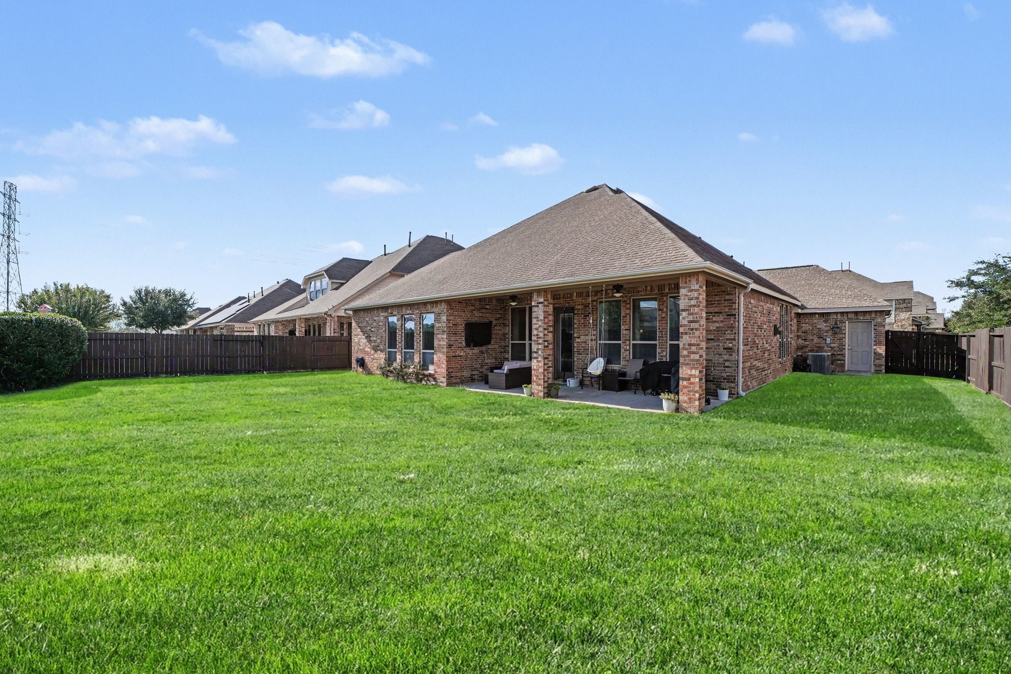Beyond the patio stretches a vibrant, lush green lawn enclosed by sturdy wooden privacy fencing on all sides, providing a safe, open space for pets, gardens, or even a future swimming pool.