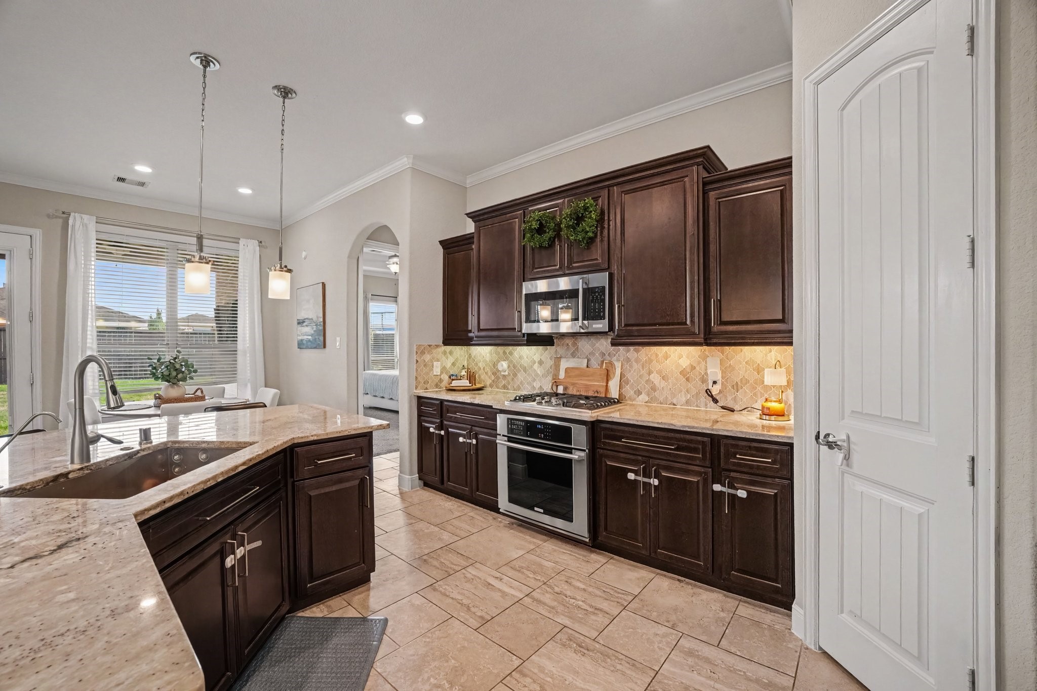Rich dark wood cabinetry provides abundant storage, beautifully contrasted by warm patterned tile backsplashes, under-cabinet lighting, and sleek stainless steel appliances, including a built-in microwave and gas range.