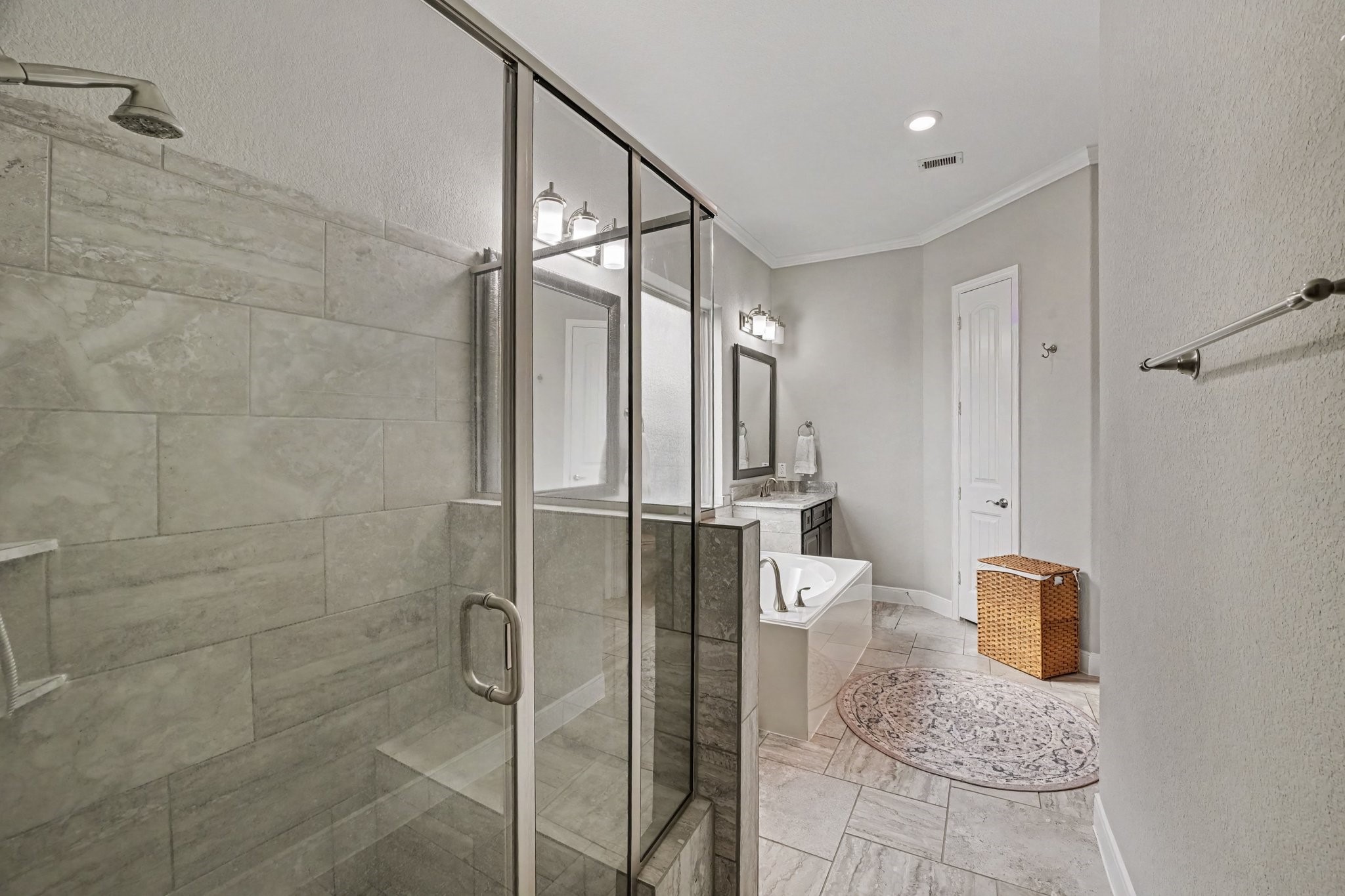 A glass-enclosed walk-in shower lined with elegant tile surrounds completes the suite, complemented by soft neutral walls, crisp white crown molding, and durable tile flooring throughout.