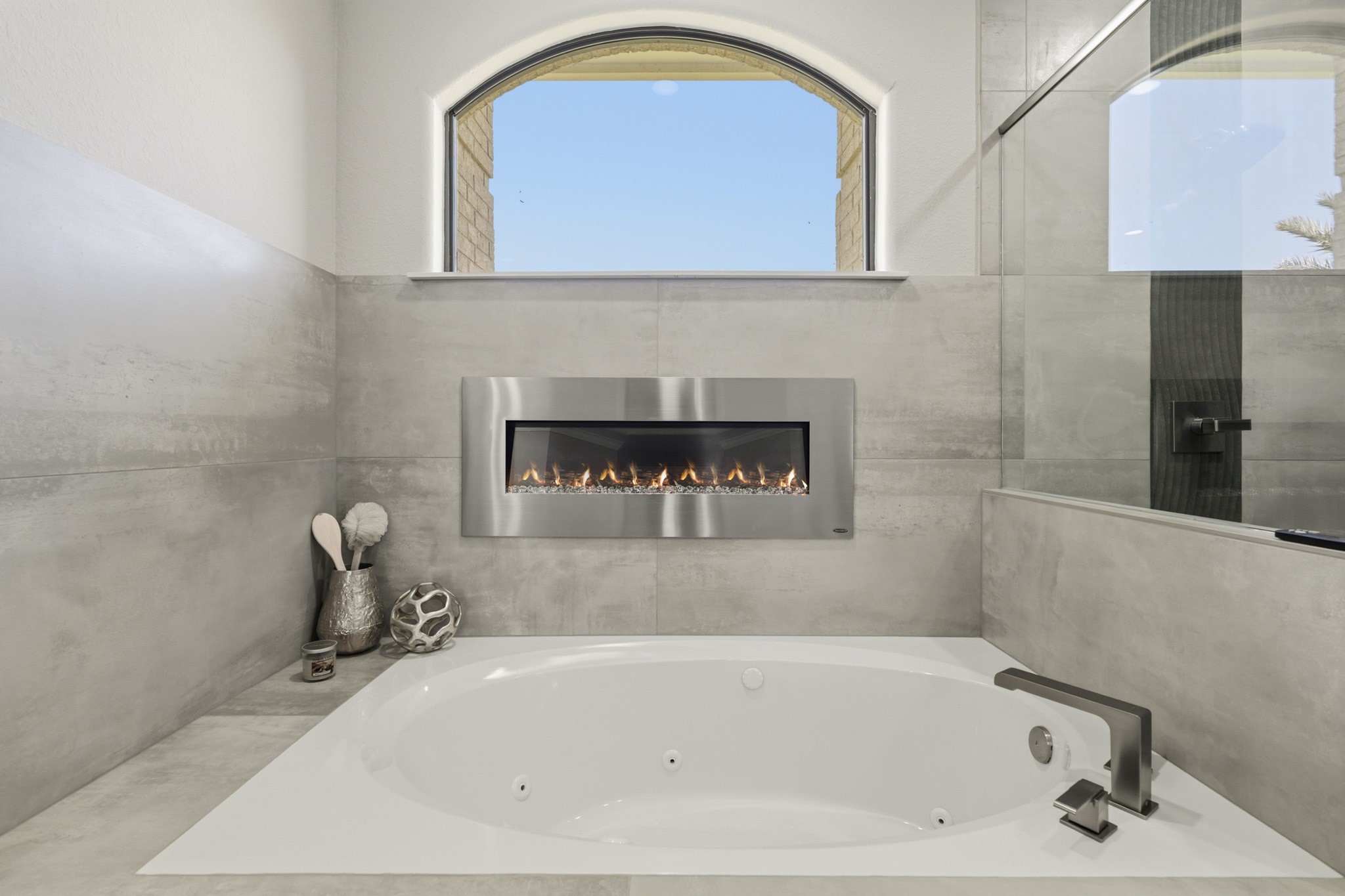 Relaxing soaking tub positioned beneath a dramatic arched window and fireplace