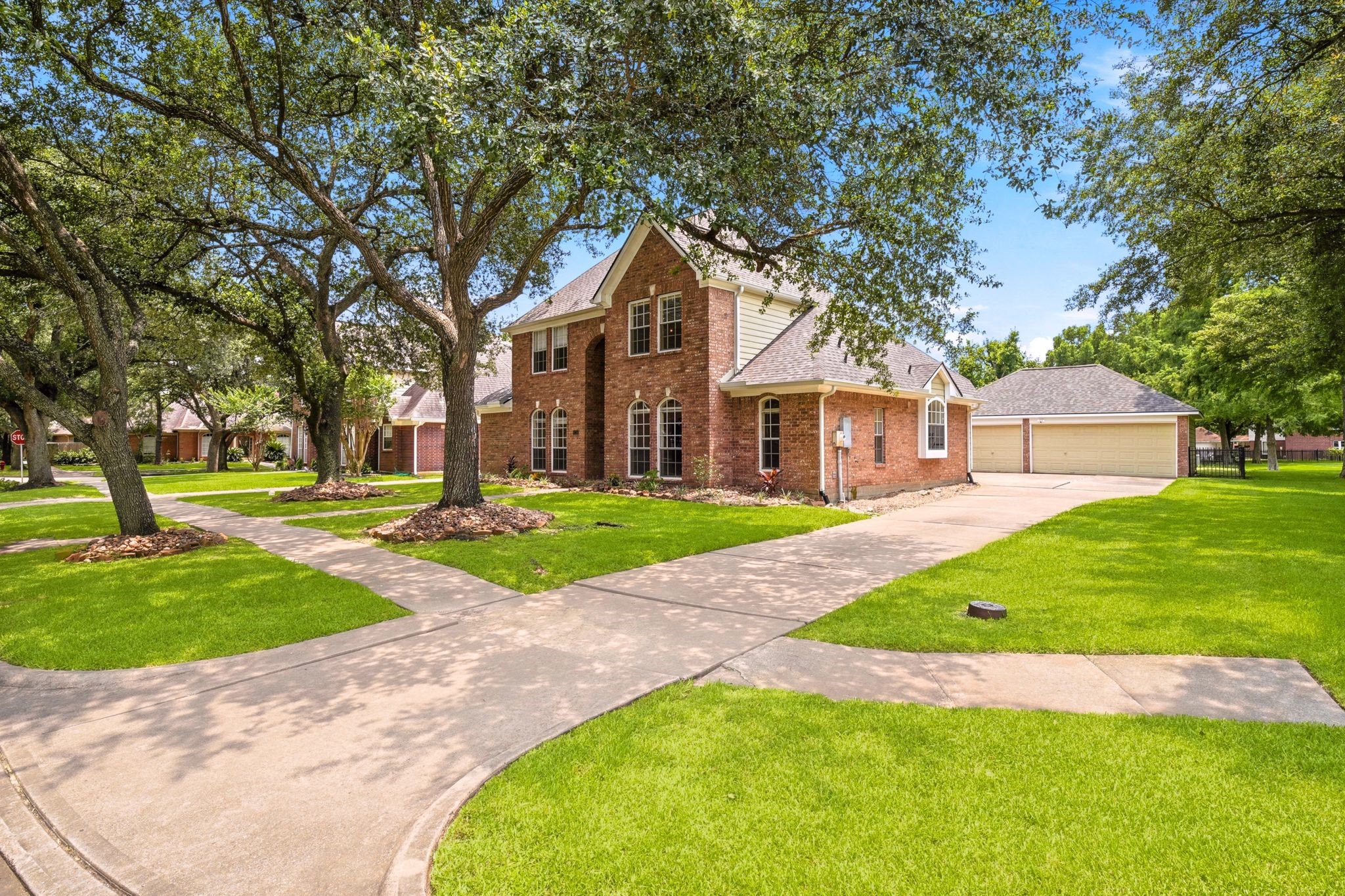 Charming two-story brick home nestled in a peaceful, suburban setting, featuring a large front yard with mature trees, a well-maintained lawn, and a paved driveway leading to a spacious attached garage.