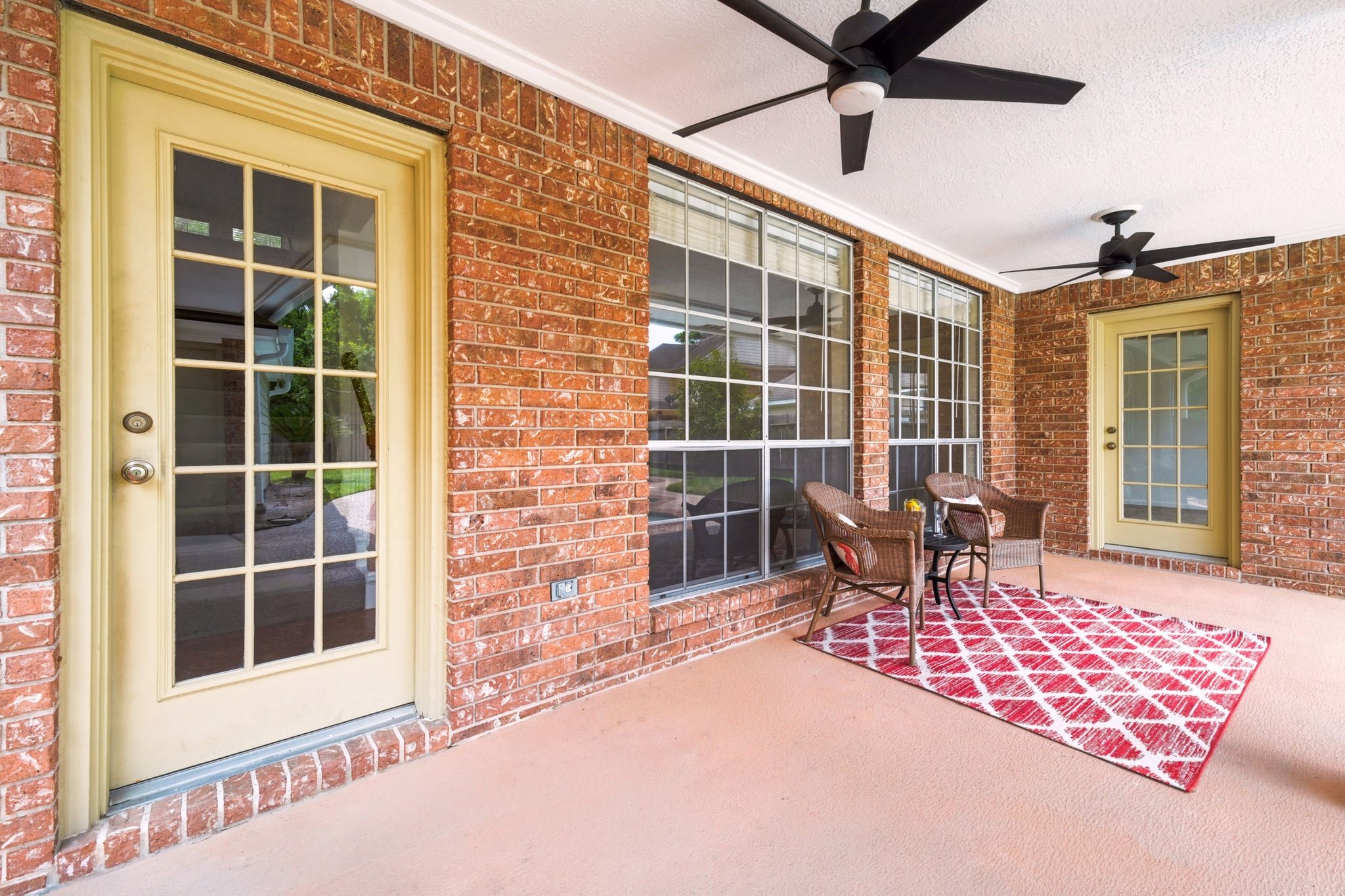 Experience relaxation on the charming covered patio, featuring elegant brick walls, two ceiling fans, and large windows for a perfect blend of comfort and style.
