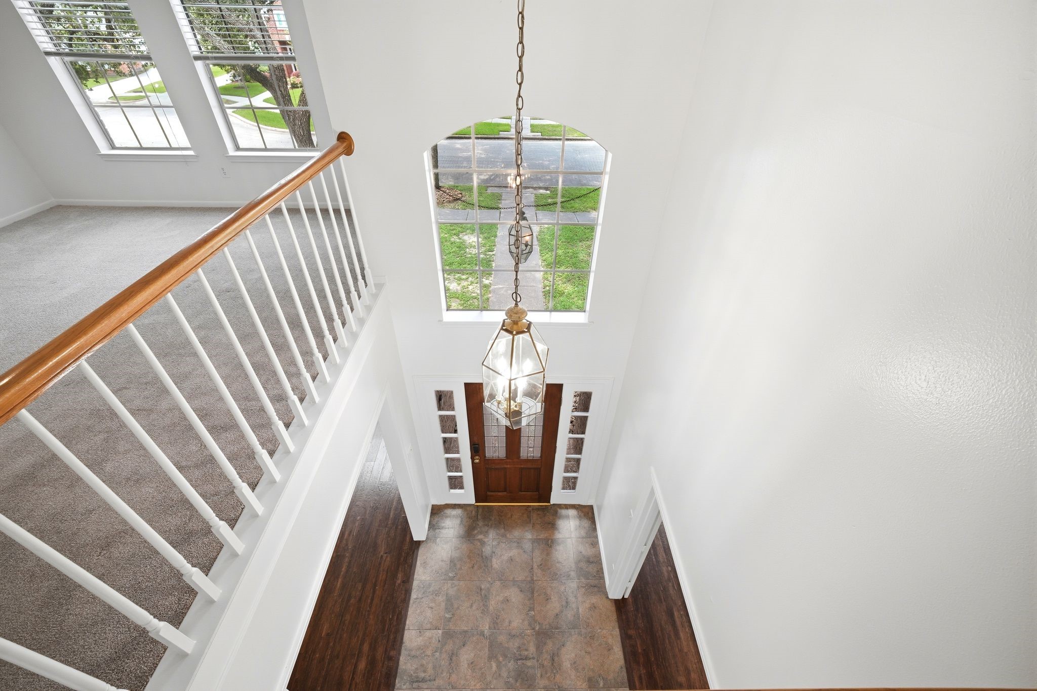 Gaze upon the elegant entry hall from above, featuring a grand chandelier and an inviting front door that floods the space with natural light through expansive windows.