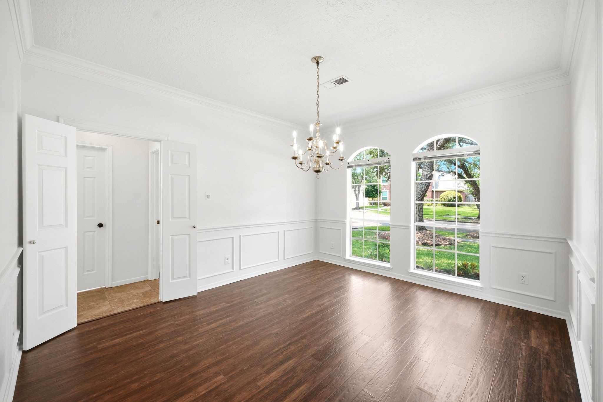 Bright and inviting, this elegant dining room boasts large windows, rich hardwood floors, and a classic chandelier, providing the perfect blank canvas for your personal touch.
