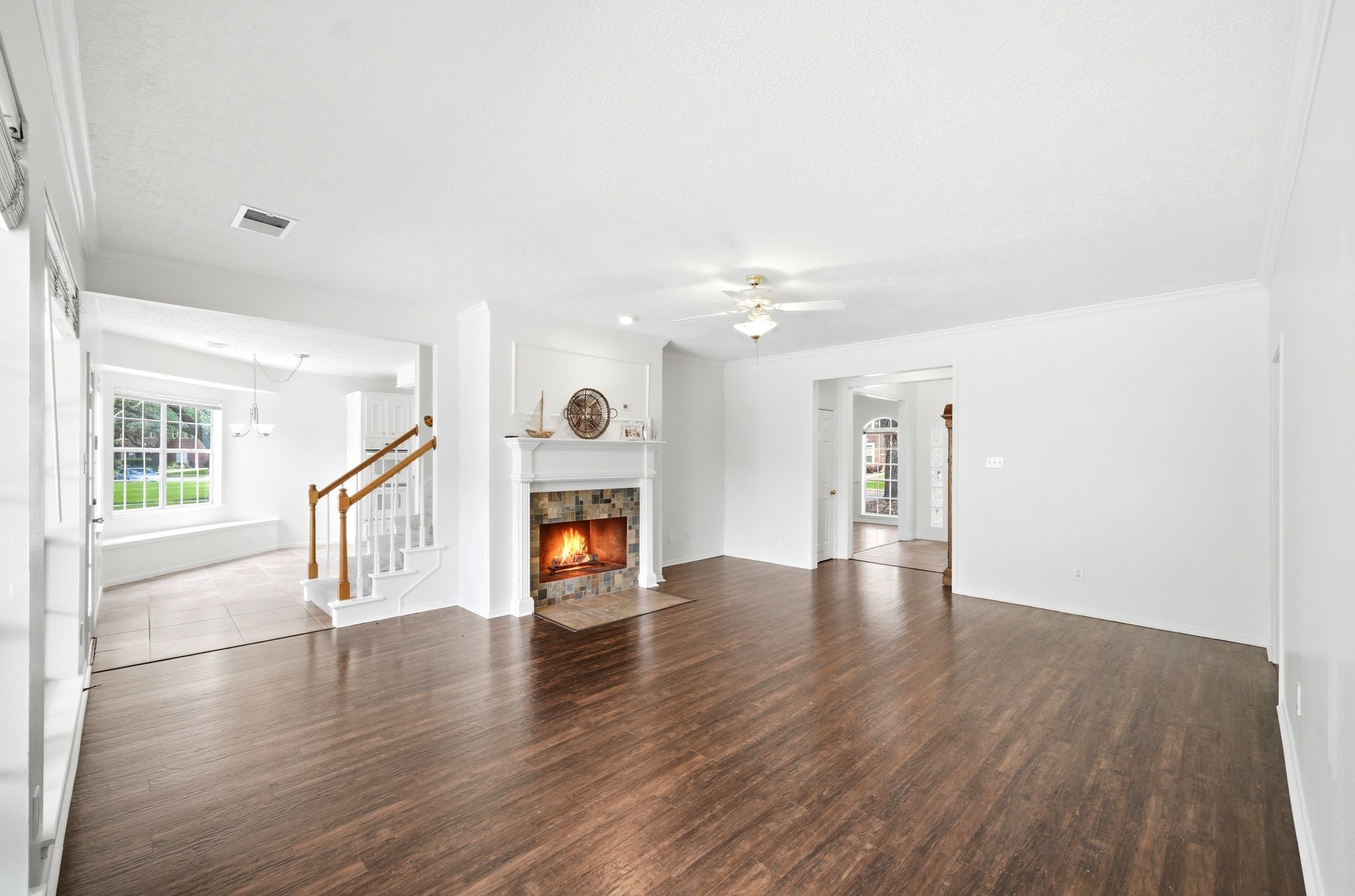 Expansive living room with elegant floors and a cozy fireplace, seamlessly connected to a tiled breakfast room and stairs leading to the inviting upstairs bedrooms.