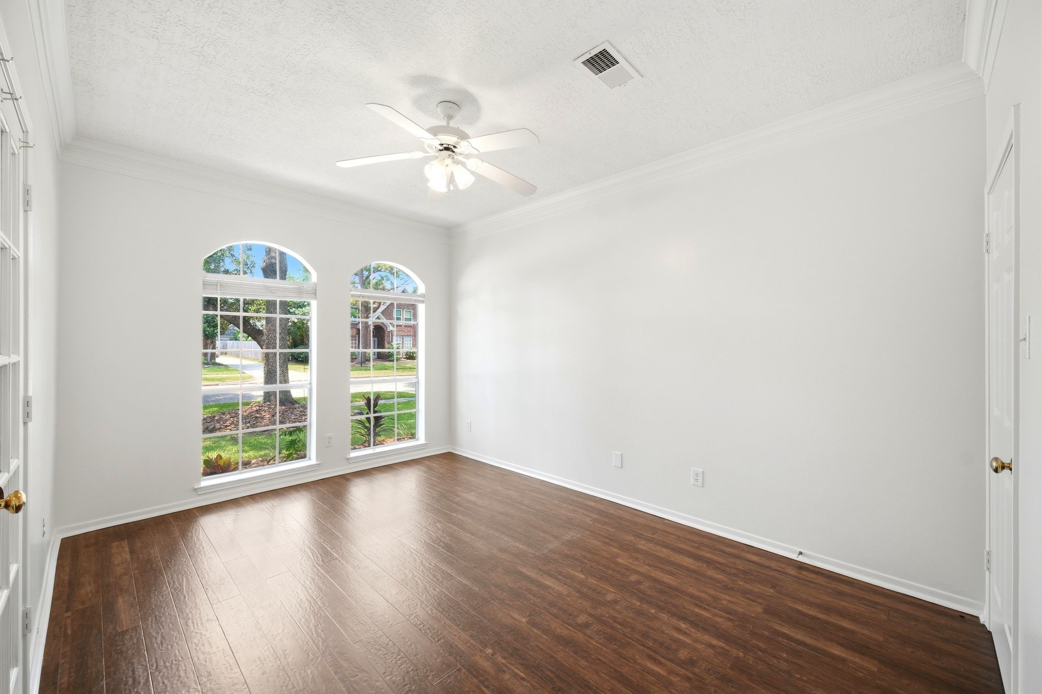 Bright and inviting, this unstaged home office features elegant wood flooring and large arched windows that flood the space with natural light, offering a serene and productive environment.