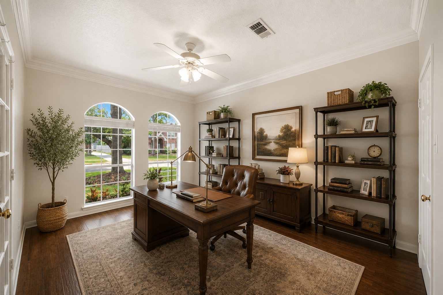 Experience productivity in this bright home office, showcasing large arched windows, a ceiling fan, and elegant wood flooring.