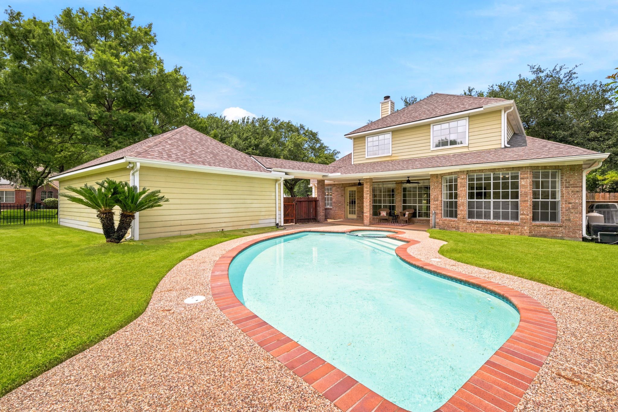 Charming two-story home with a spacious backyard oasis, featuring a sparkling pool nestled among lush grass and mature trees, and a covered patio perfect for outdoor relaxation and entertaining.