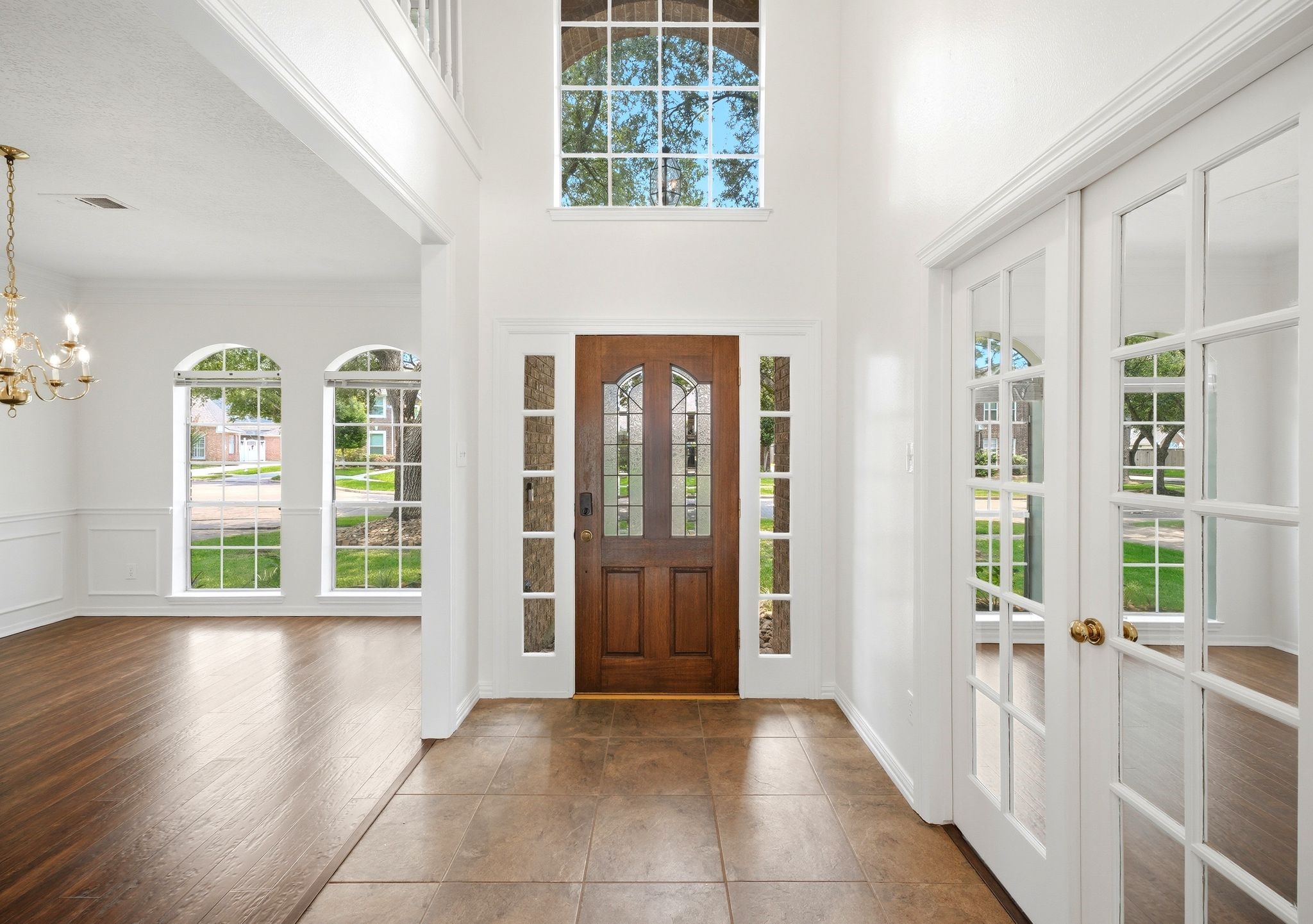 Step into a stunning entryway with soaring ceilings and abundant natural light, featuring a stylish wooden front door with glass panels and elegant French doors leading to the formal dining room and home office.