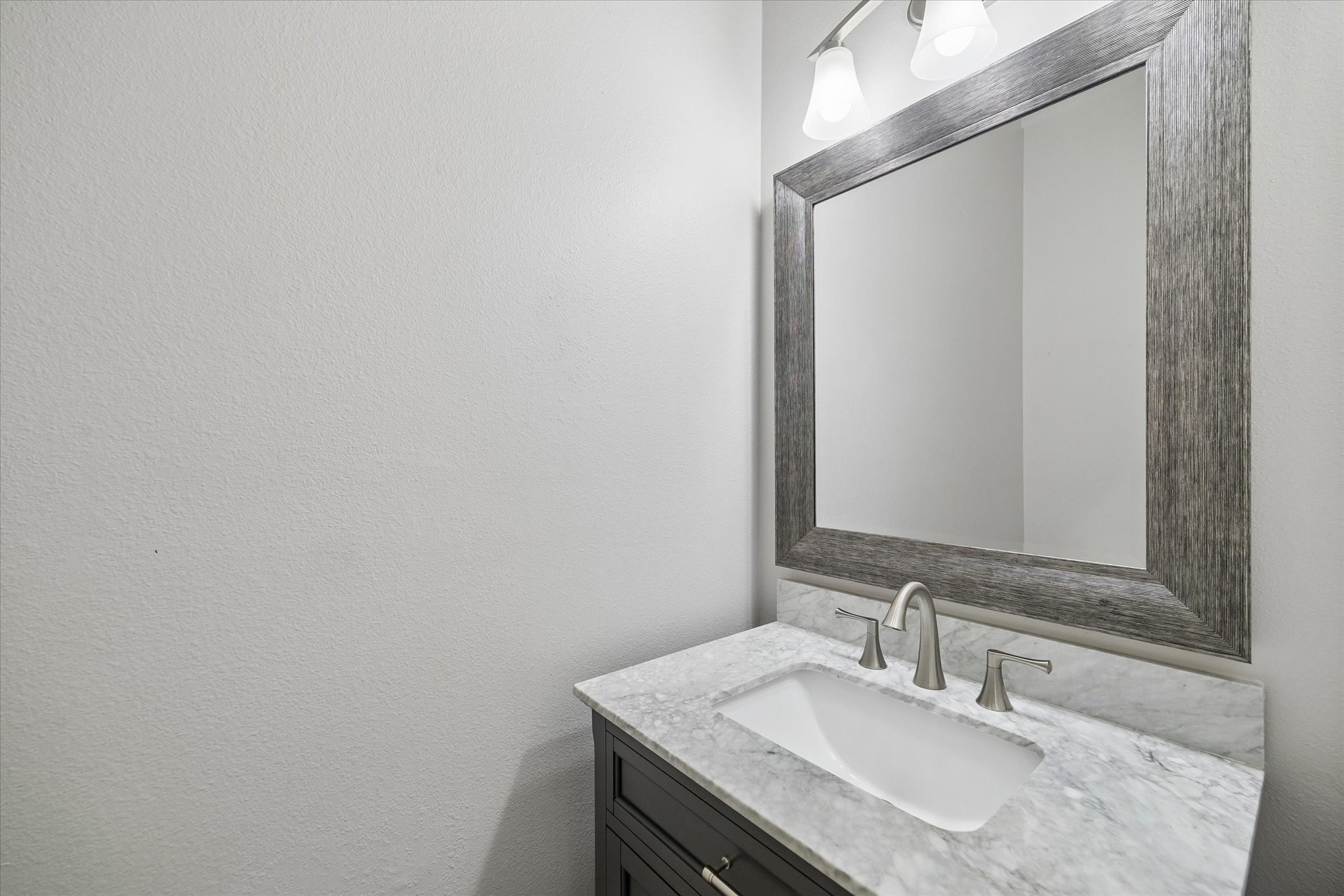 A half-bath is conveniently located on the first floor and features an updated vanity, faucet, framed mirror, and lighting.