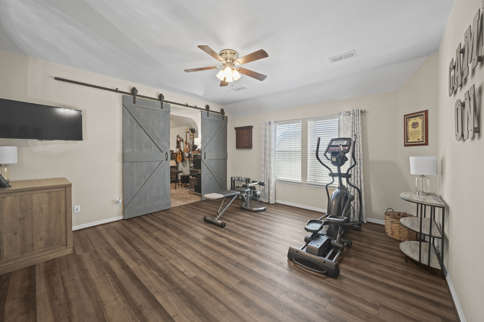 Spacious home gym with stylish barn doors, wood flooring, and ample natural light from large windows, perfect for workouts and relaxation.