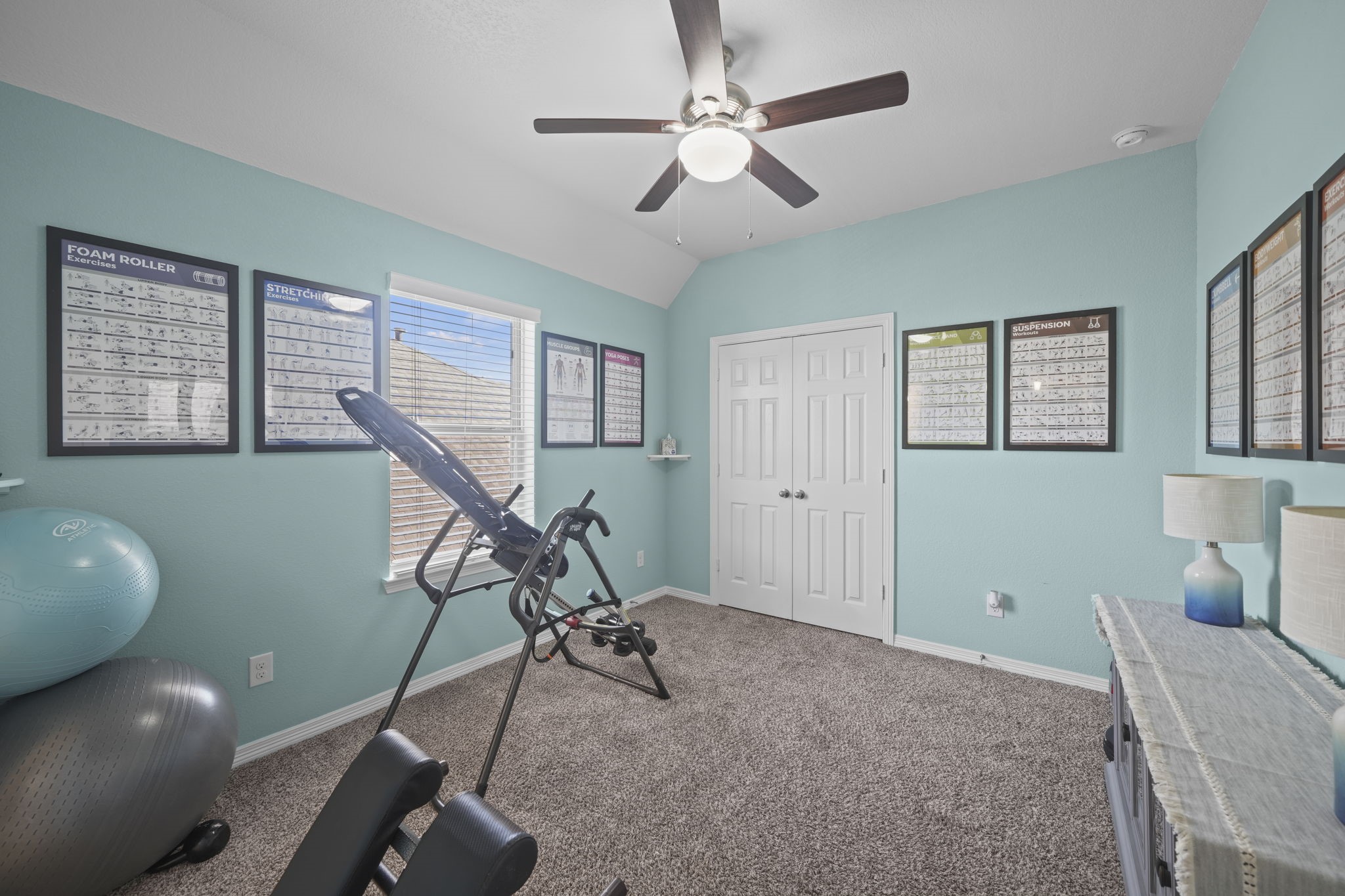 Bright and inviting exercise room featuring a ceiling fan, ample natural light, and motivational wall posters, perfect for home workouts.