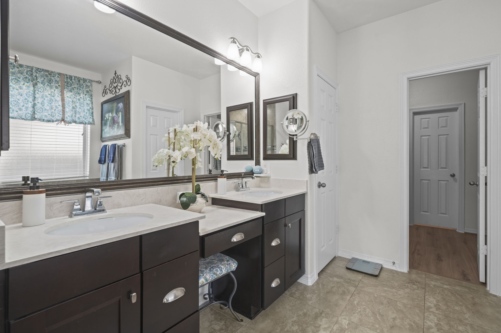 Elegant bathroom featuring a double vanity with dark cabinetry and ample countertop space, complemented by a large mirror and stylish lighting.