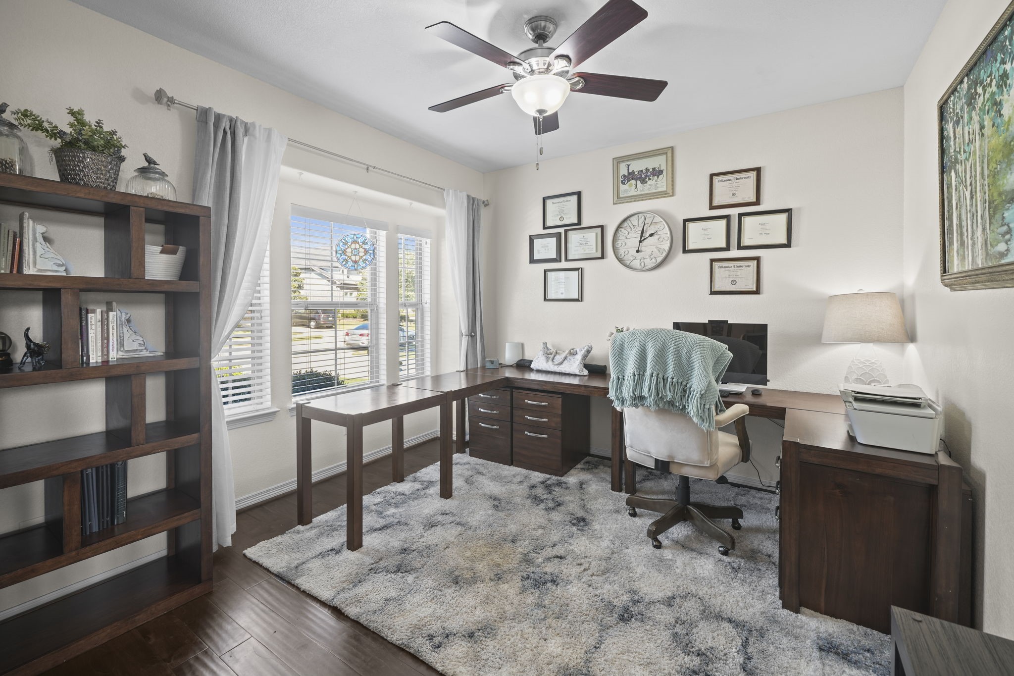 Bright and inviting home office featuring large windows, elegant wood flooring, and a stylish desk setup complemented by ample shelving and tasteful decor.