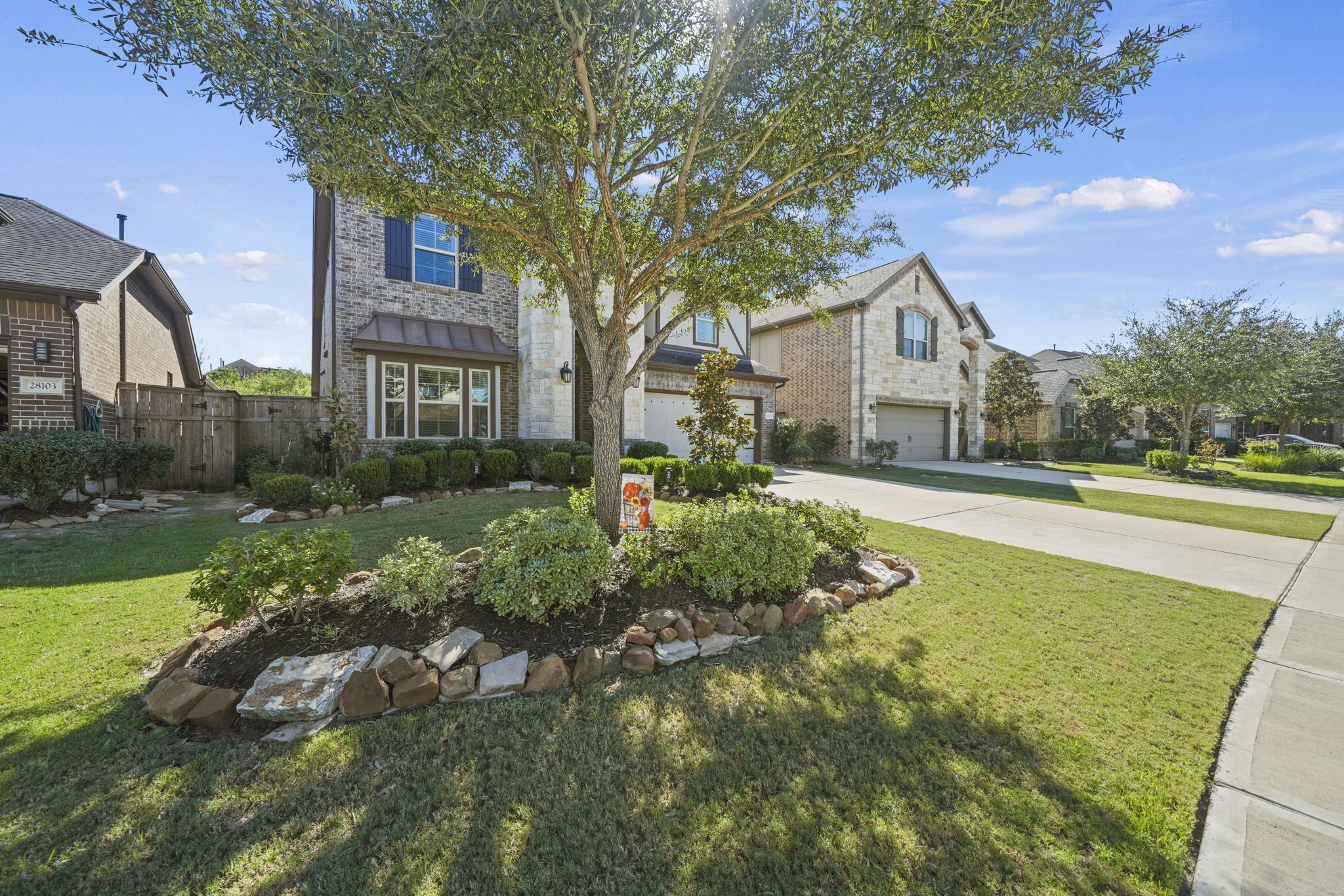 Charming two-story home with a beautifully landscaped front yard featuring a mature tree and well-maintained shrubs, set in a peaceful neighborhood.