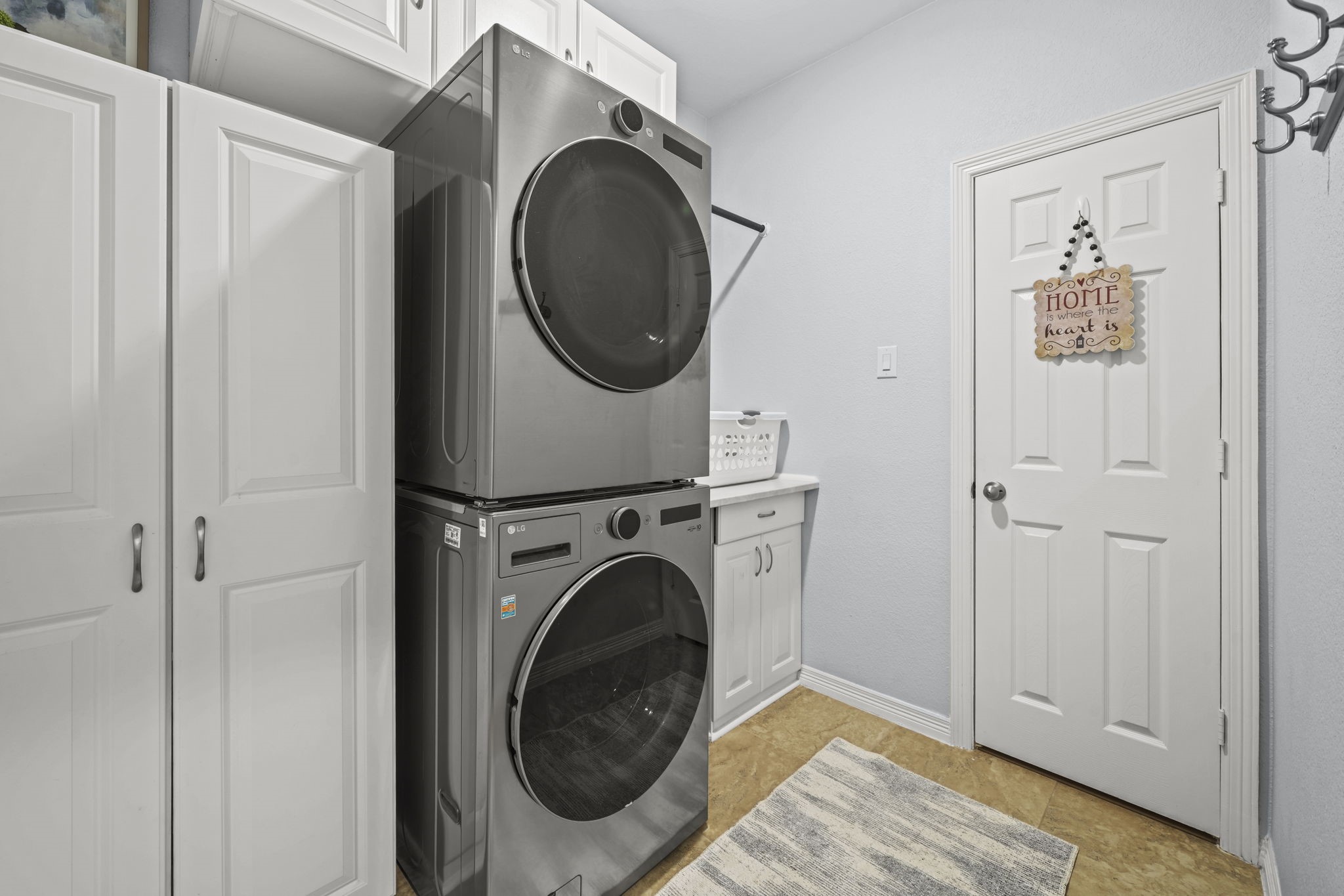 Efficient laundry room featuring modern stacked washer and dryer, ample cabinetry for storage, and a convenient folding counter.