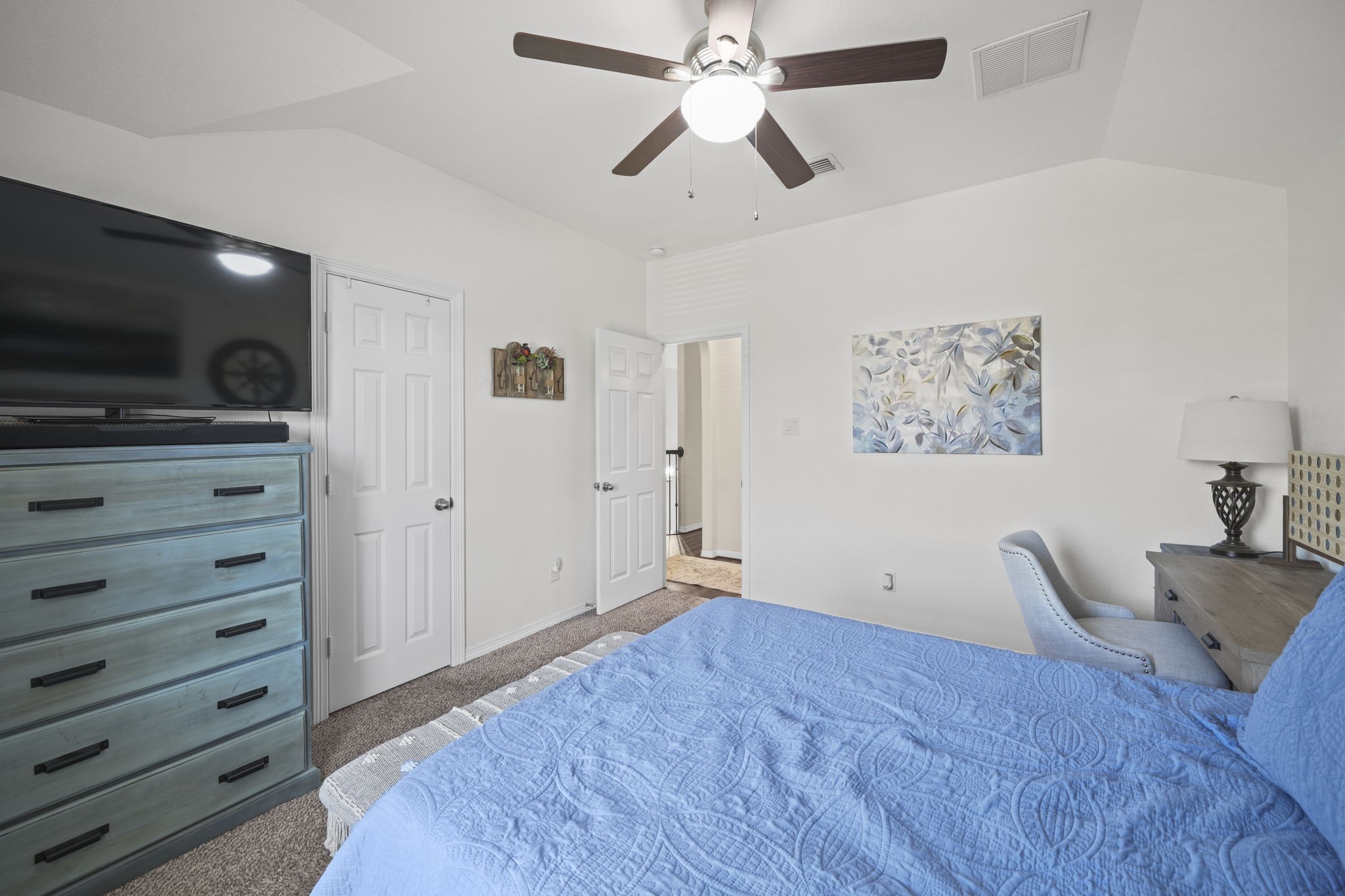 Bright and inviting bedroom featuring a vaulted ceiling, modern ceiling fan, and ample space with a stylish dresser and cozy workspace.