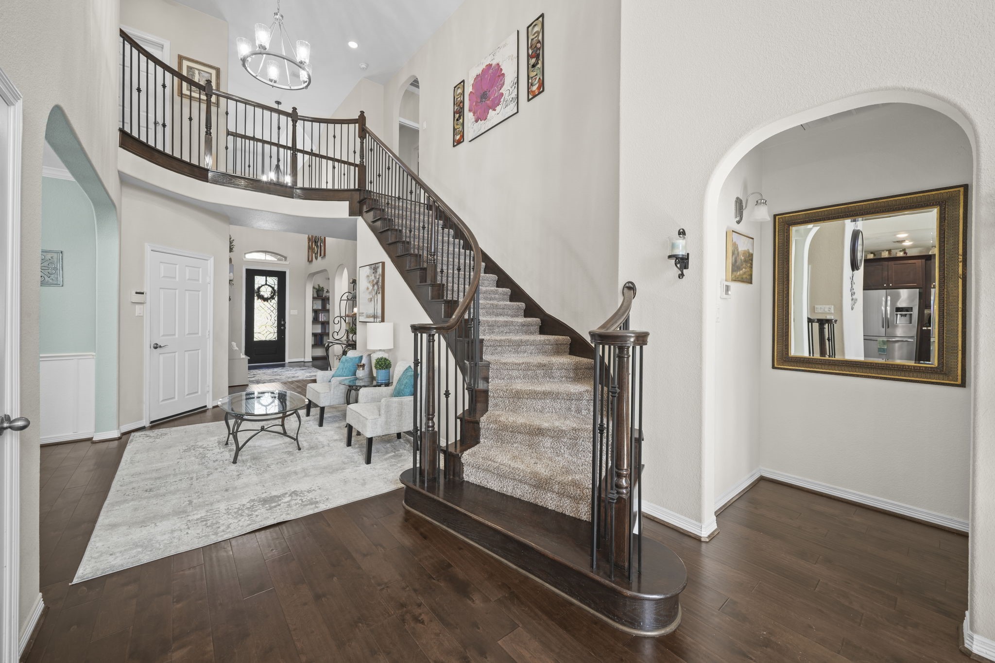 Elegant foyer with a grand curved staircase, rich hardwood floors, and an inviting living area perfect for entertaining.