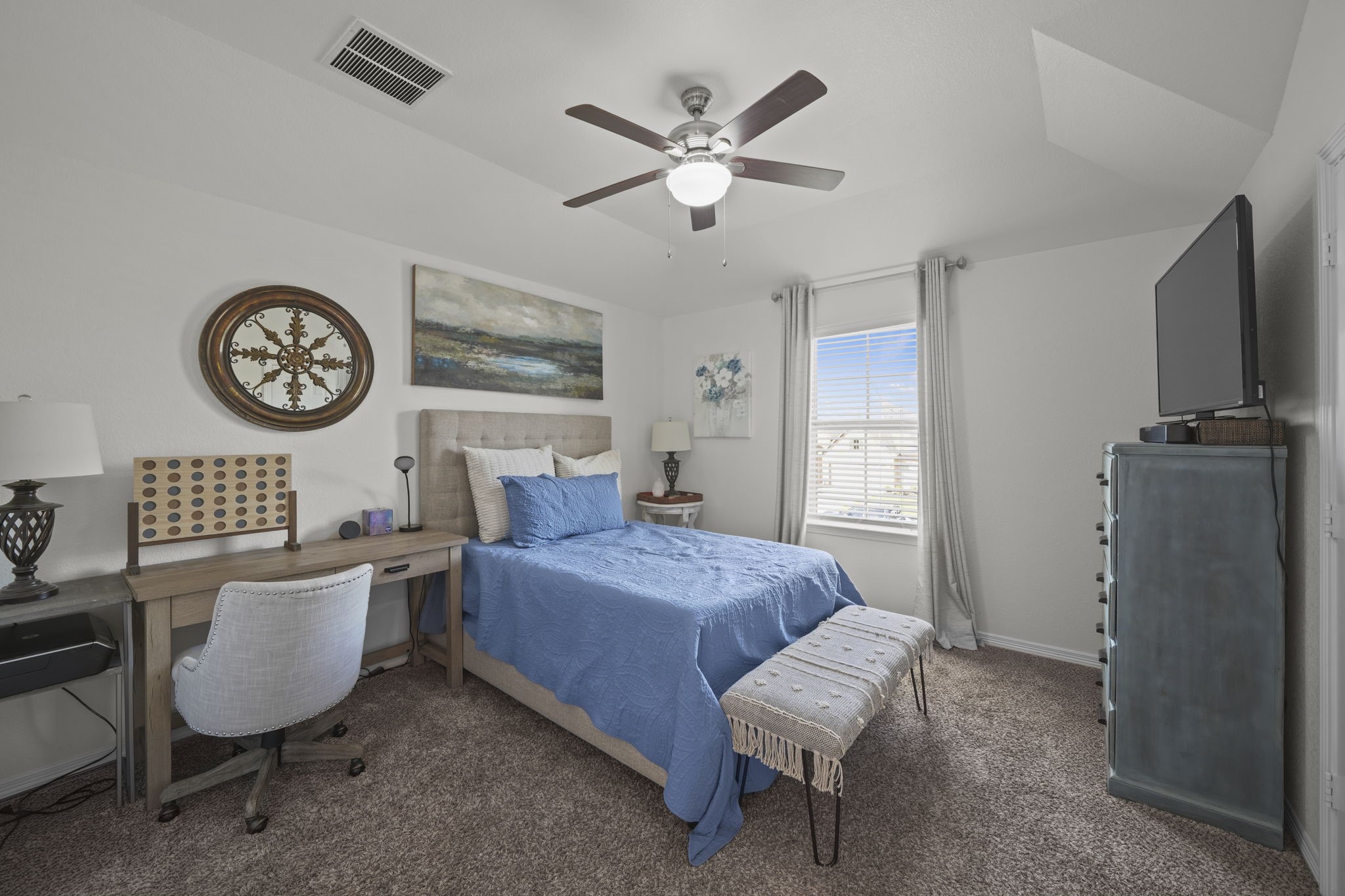 Cozy bedroom with a soft blue palette, featuring a comfortable bed, stylish decor, and ample natural light through a large window, perfect for relaxation.