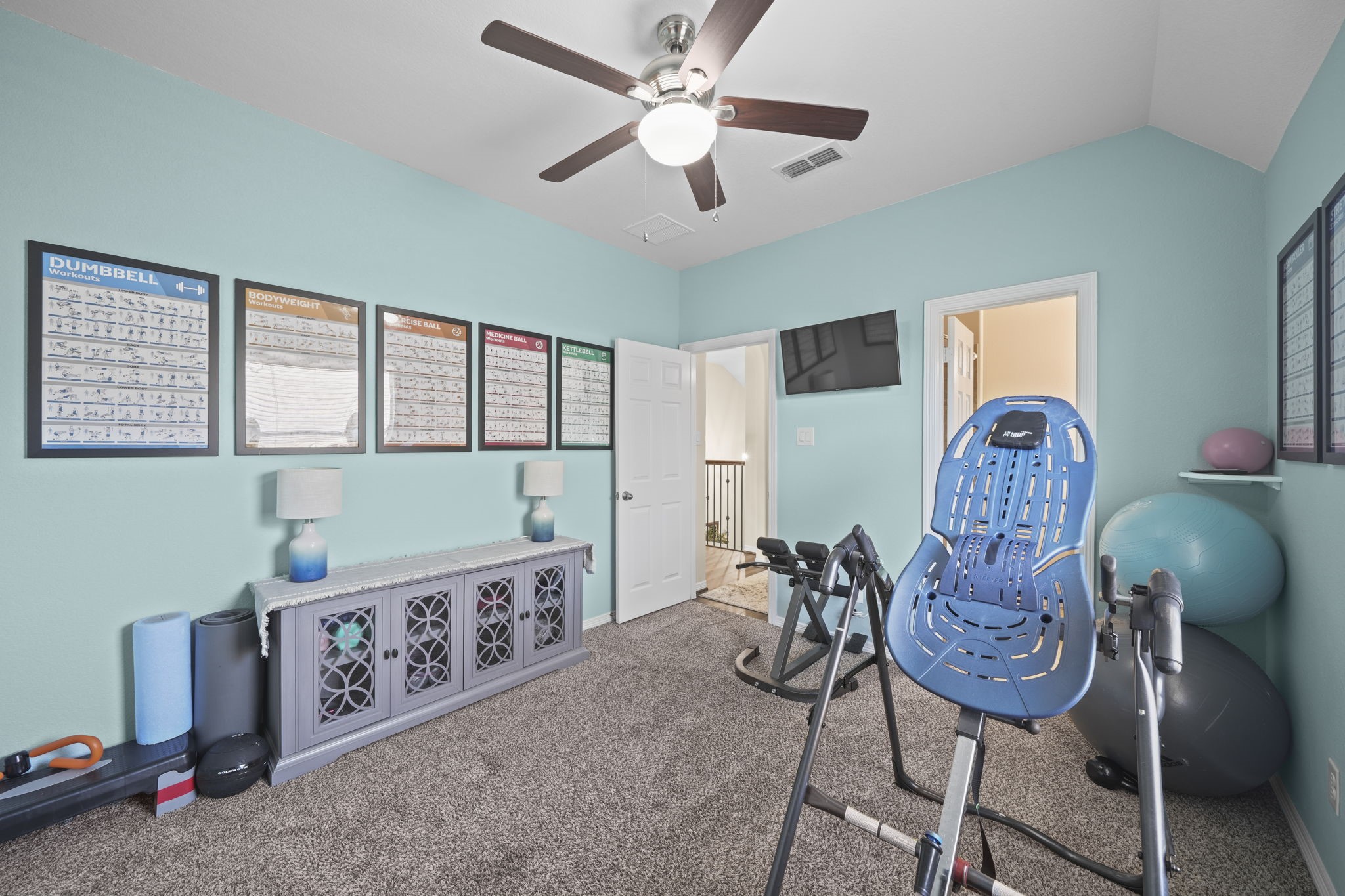 Bright and airy home gym with modern equipment, exercise guides, and a ceiling fan, perfect for fitness enthusiasts.