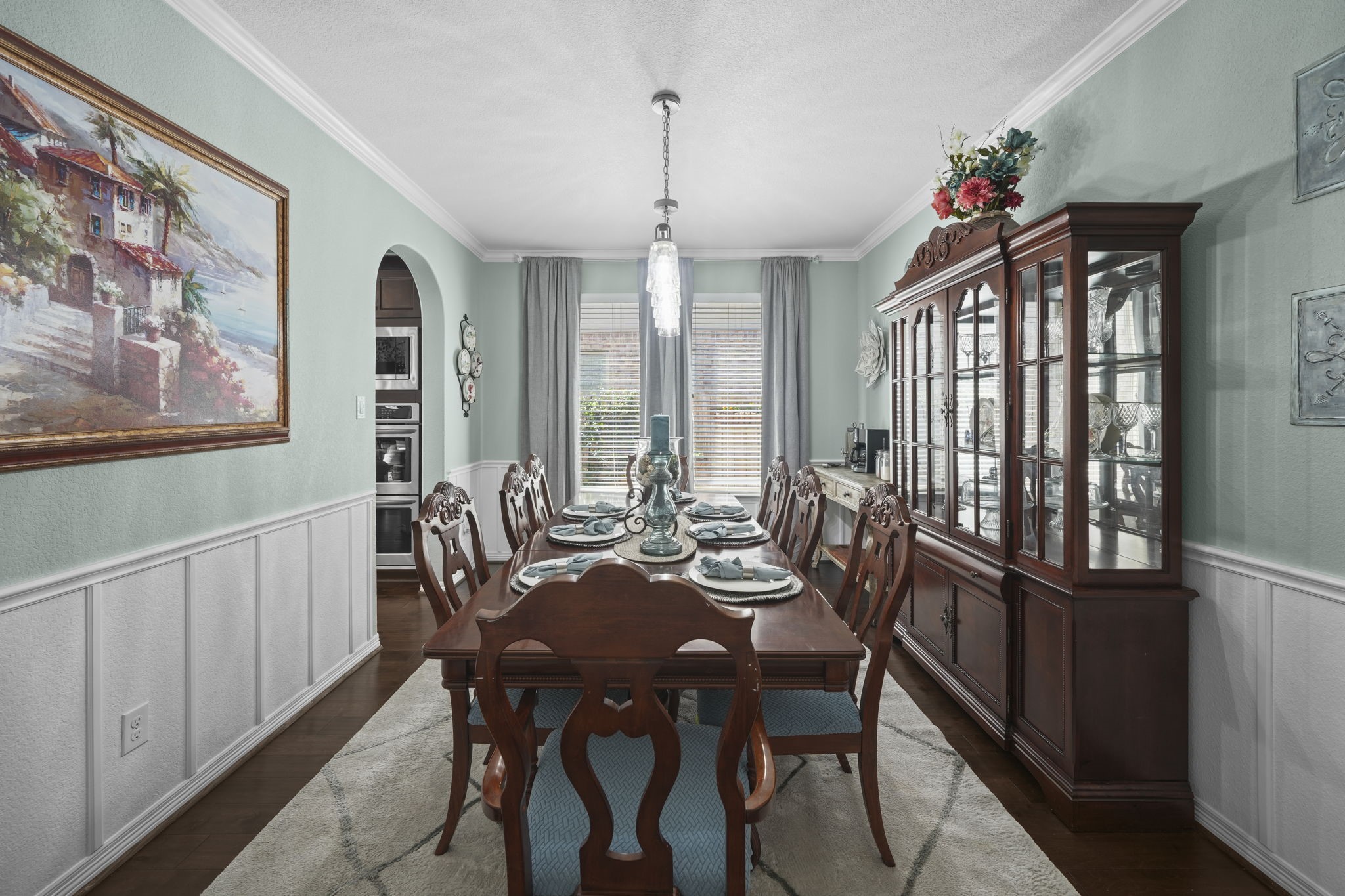 Elegant dining room featuring a classic wooden table set, a sophisticated china cabinet, and tasteful wall art, all illuminated by natural light from large windows.