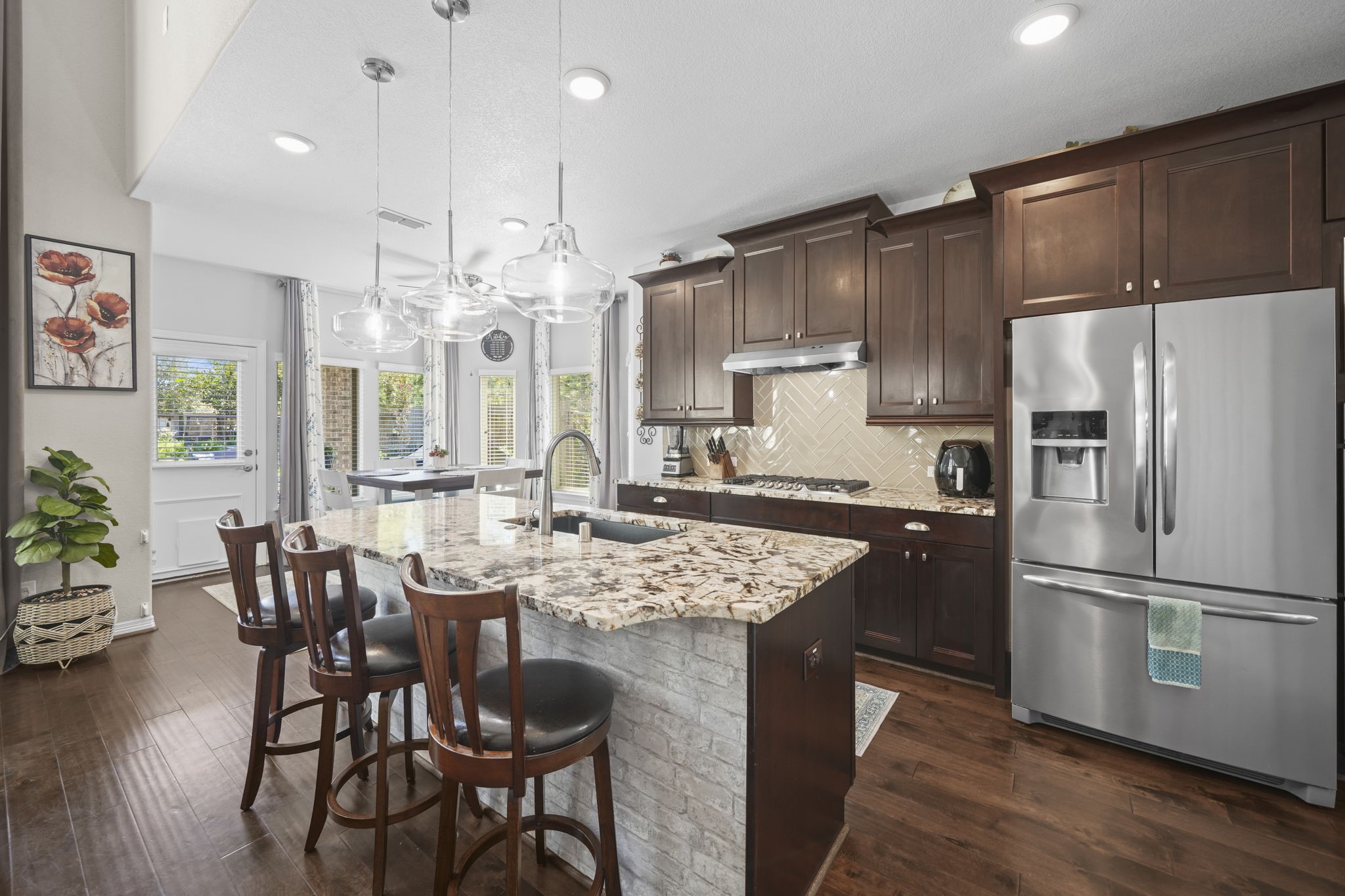Elegant kitchen featuring rich wooden cabinetry, a large granite island with seating, and modern stainless steel appliances, all under stylish pendant lighting.