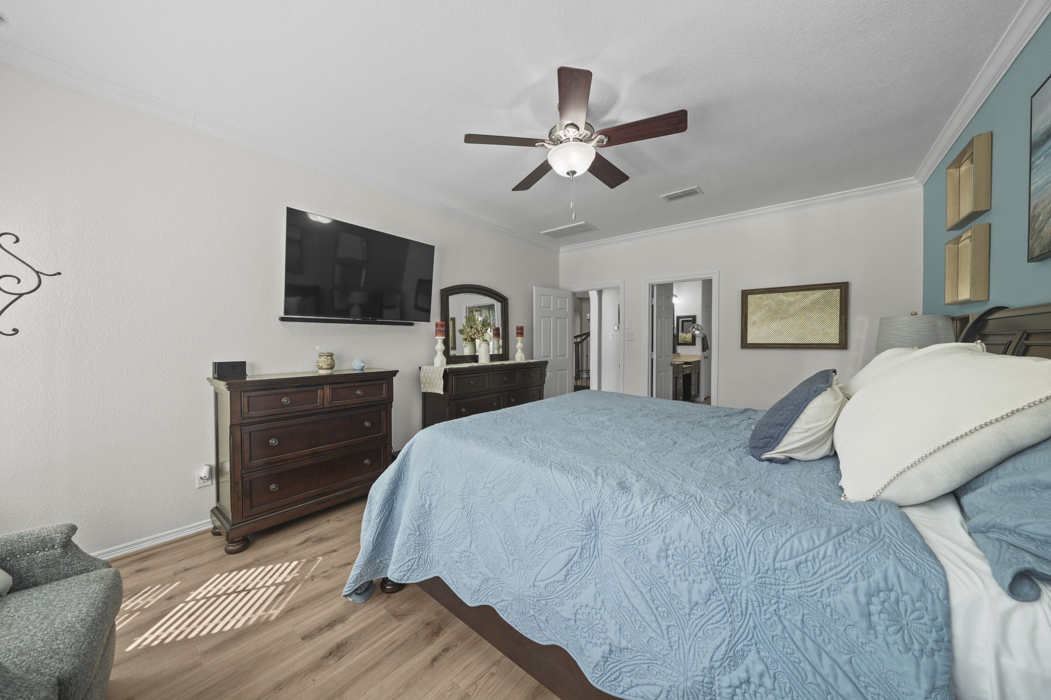 Spacious bedroom featuring a cozy blue bedding set, elegant wooden furniture, and a ceiling fan, creating a relaxing retreat.