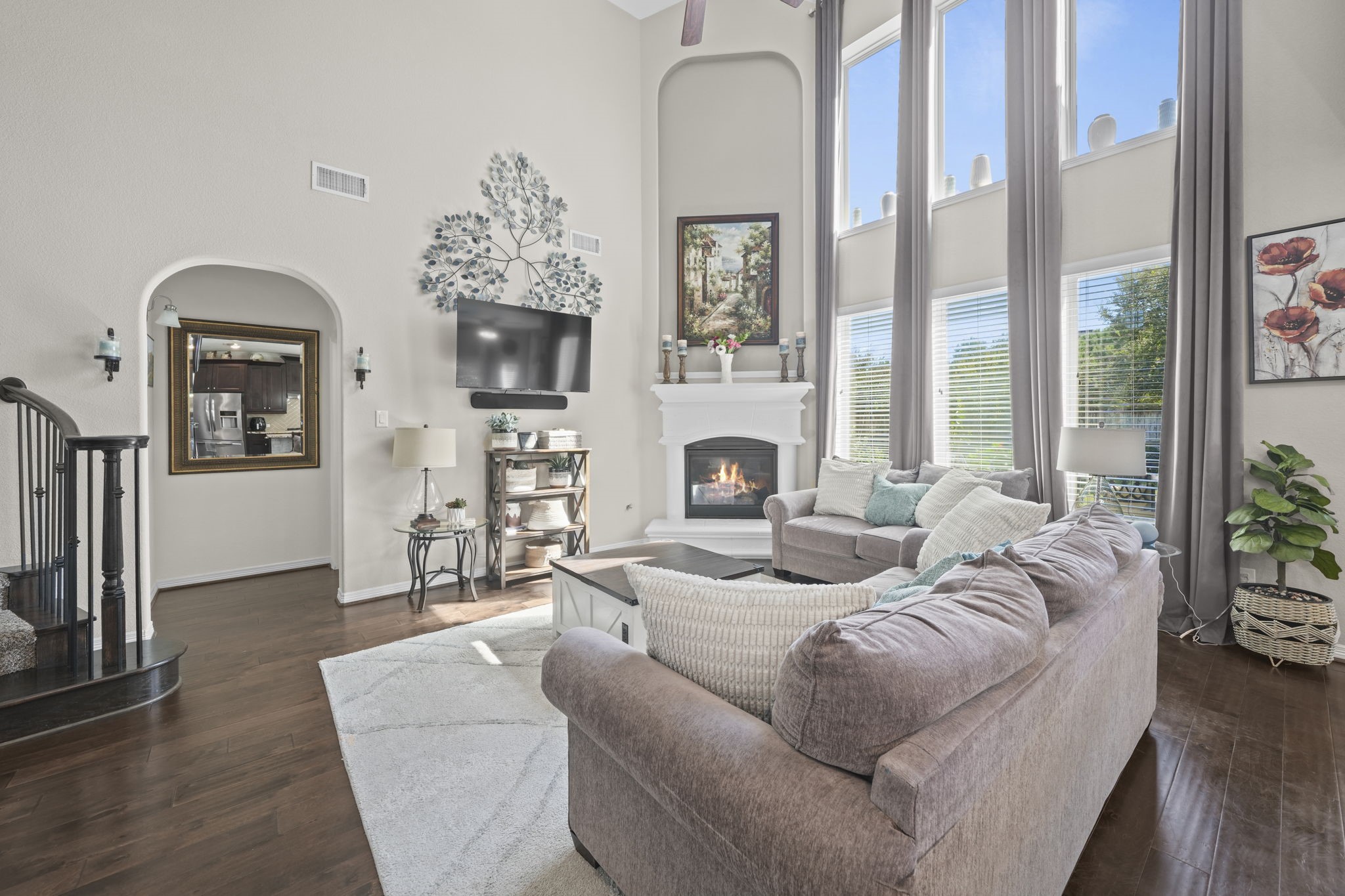 Spacious living room with soaring ceilings, a cozy fireplace, and abundant natural light from large windows, creating a welcoming and elegant atmosphere.