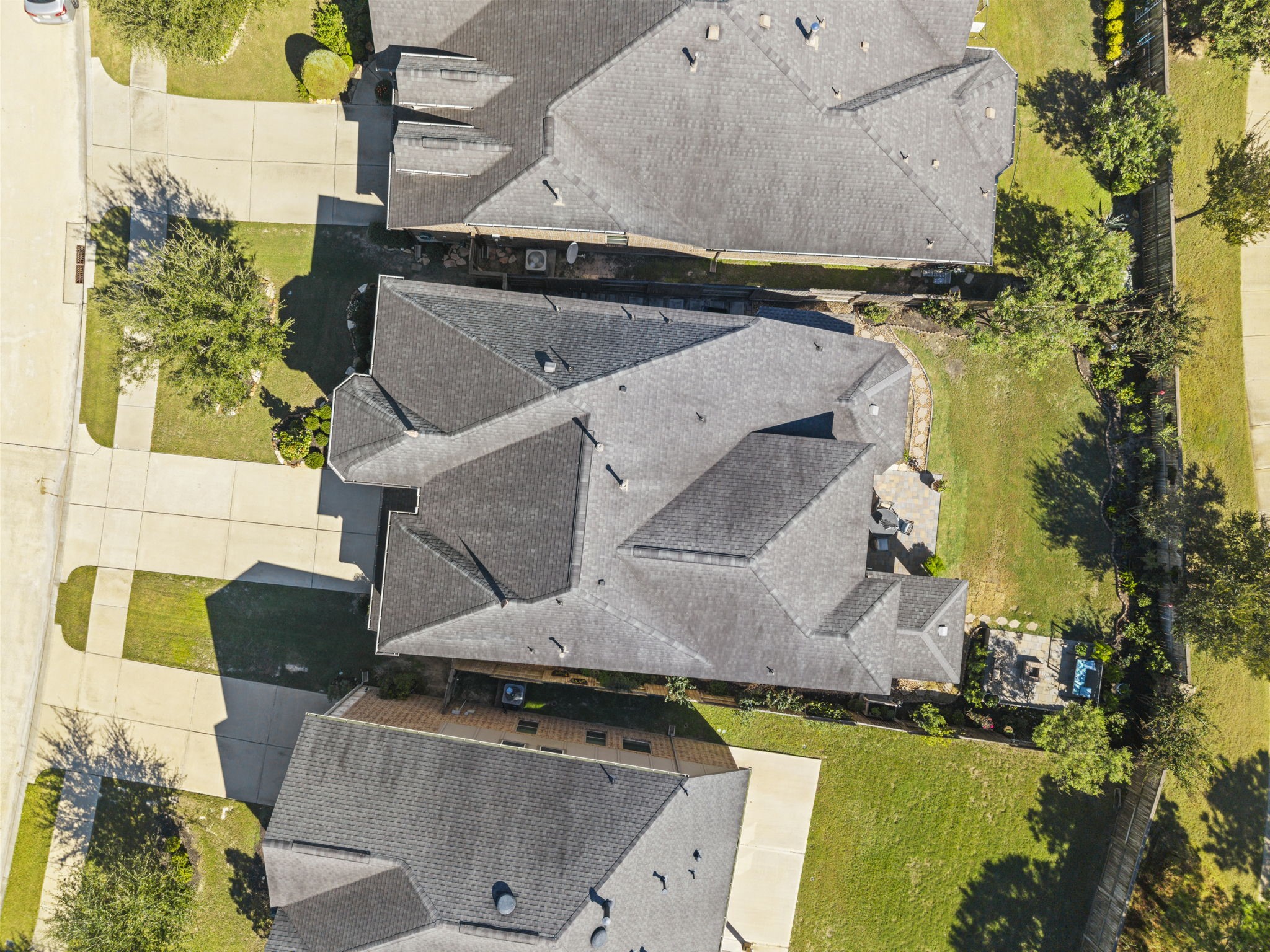 Aerial view of a spacious property featuring a large, well-maintained roof and expansive driveways, surrounded by lush greenery and a fenced backyard, offering ample outdoor space.